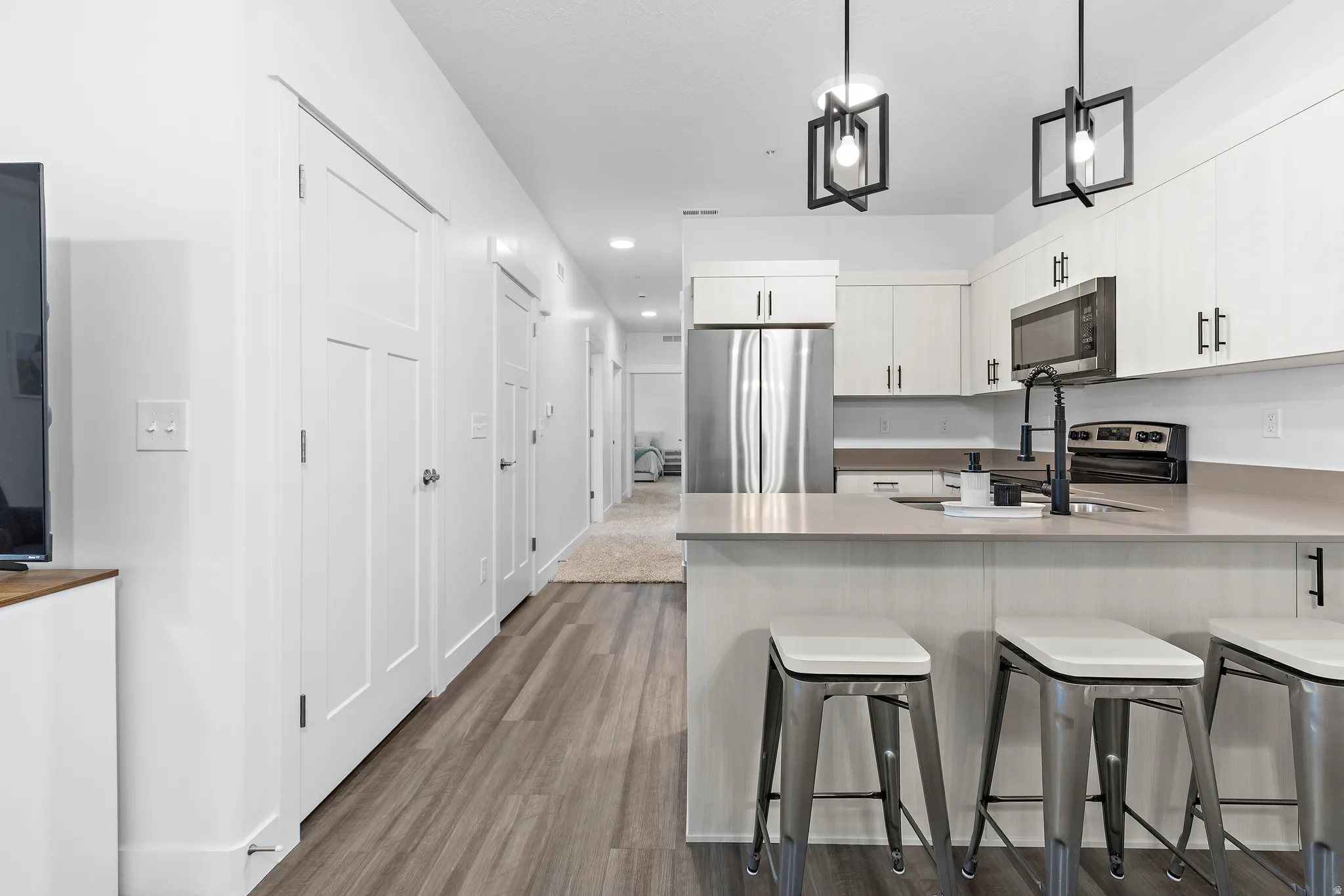 Kitchen featuring pendant lighting, stainless steel appliances, a peninsula, a breakfast bar area, and dark wood-style floors