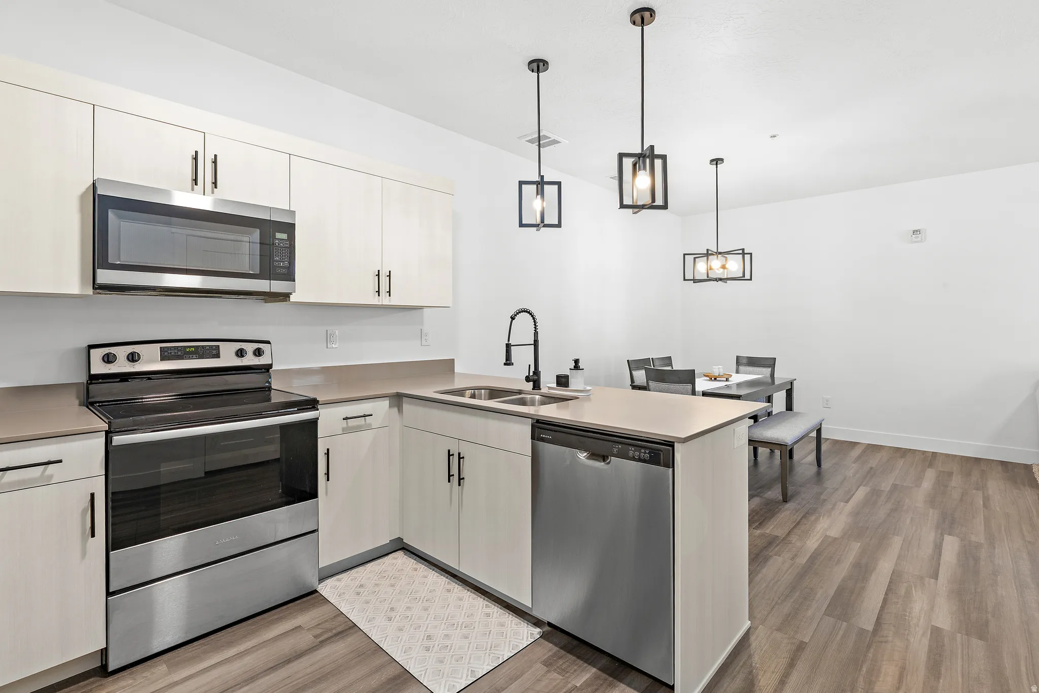Kitchen with stainless steel appliances, light wood-style flooring, a peninsula, and light countertops