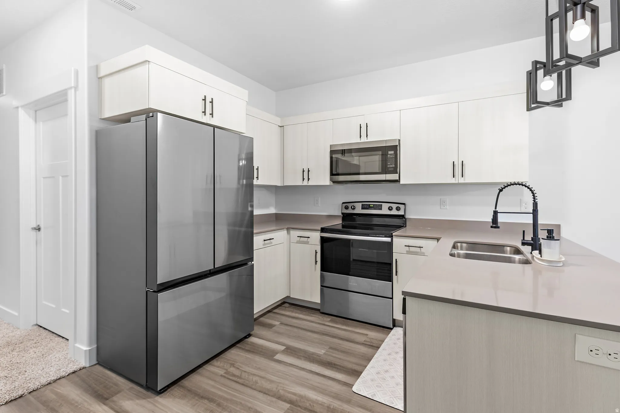 Kitchen with stainless steel appliances, hanging light fixtures, a peninsula, light wood-style flooring, and light stone counters