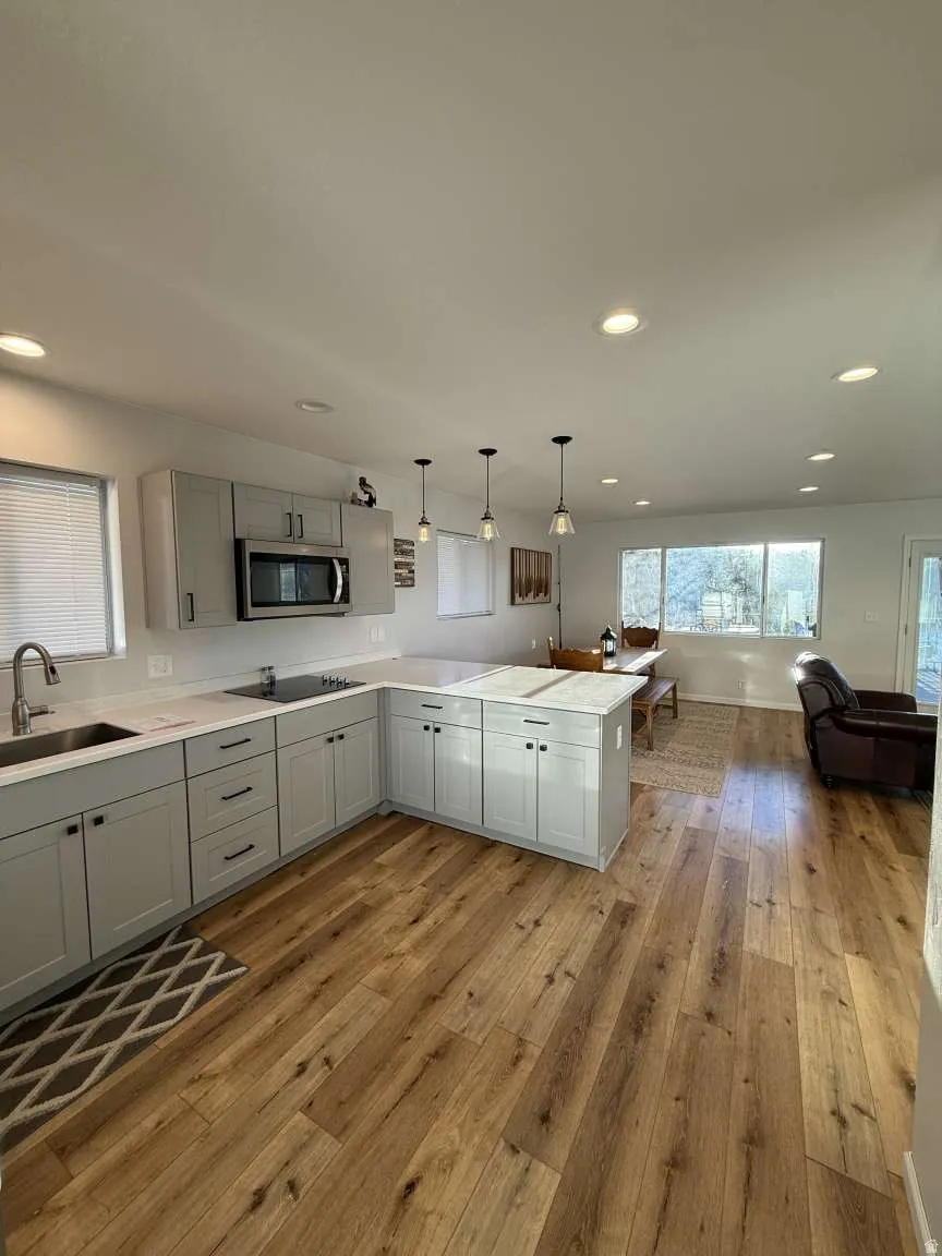 Kitchen with decorative light fixtures, gray cabinets, a peninsula, light wood finished floors, and open floor plan