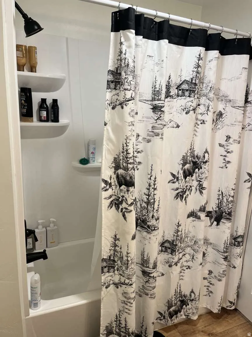 Bathroom with shower / bathtub combination with curtain and wood finished floors