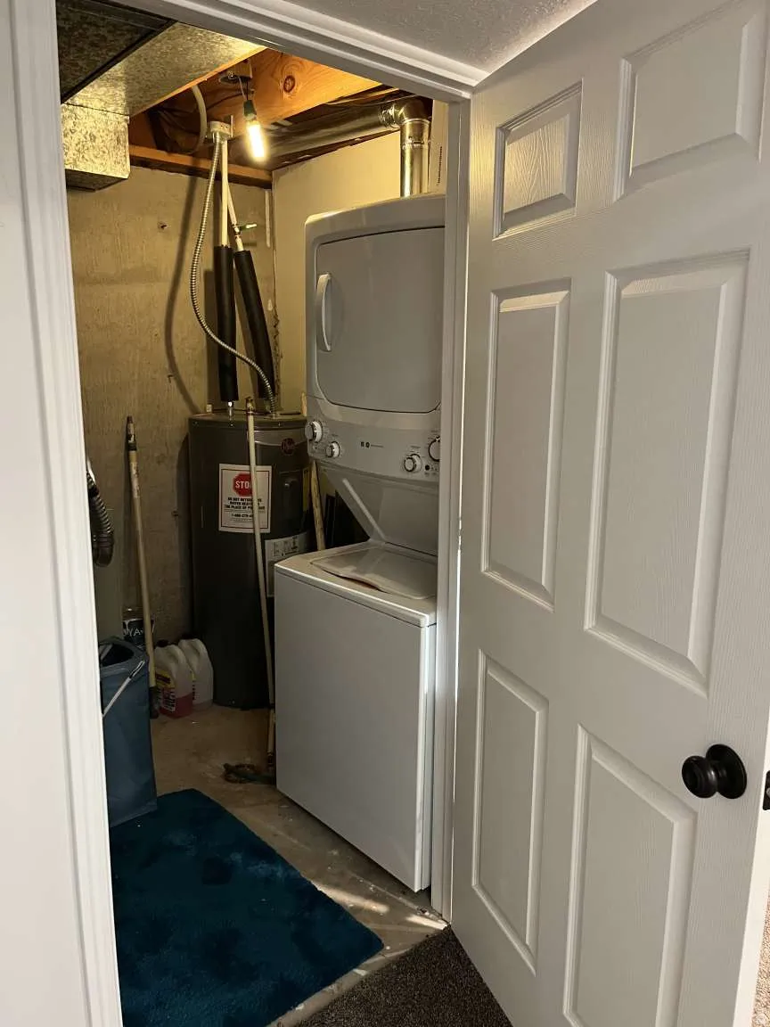 Laundry area with stacked washer and clothes dryer, electric water heater, and unfinished concrete floors