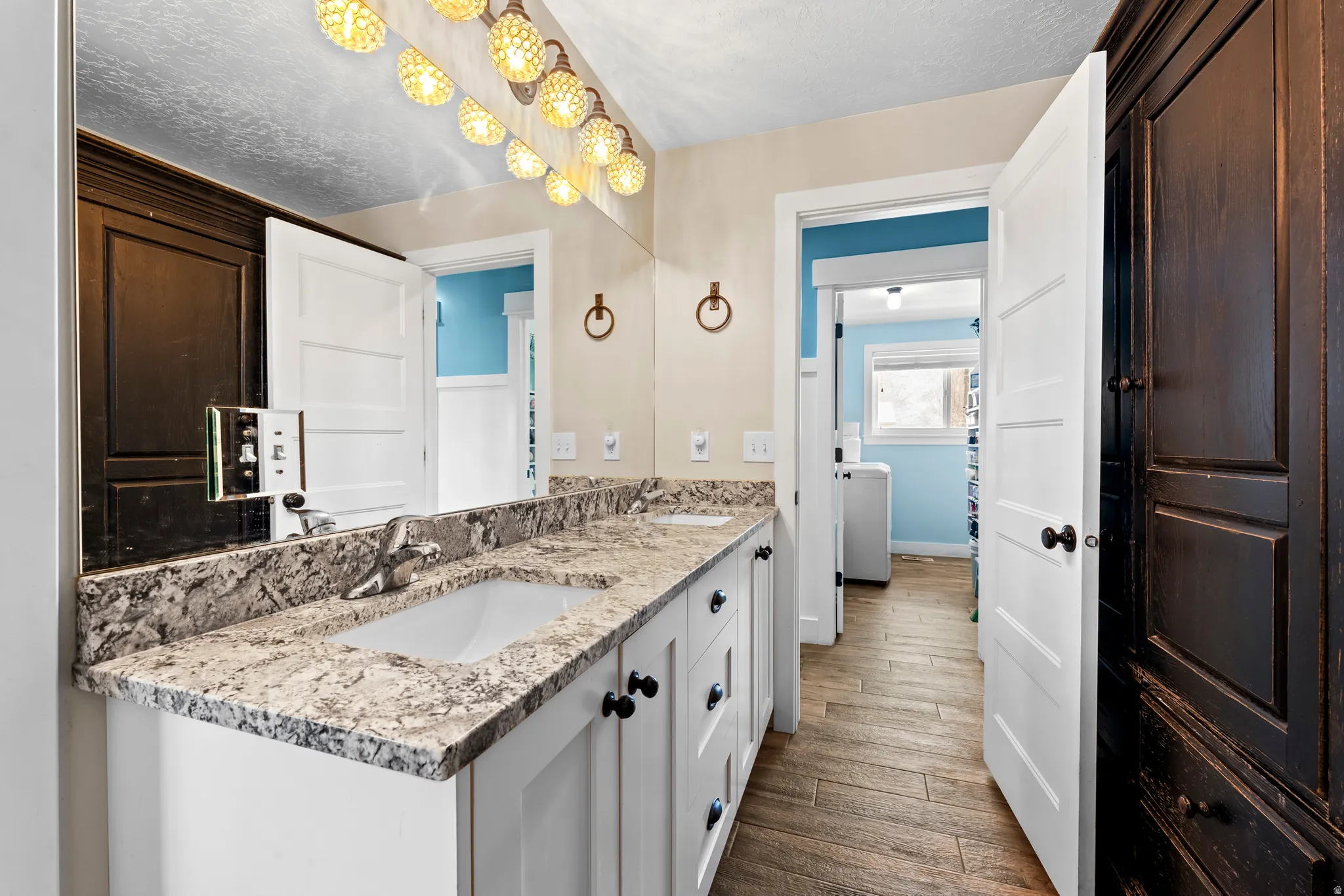 Full bath with double vanity, dark wood-style floors, and a textured ceiling