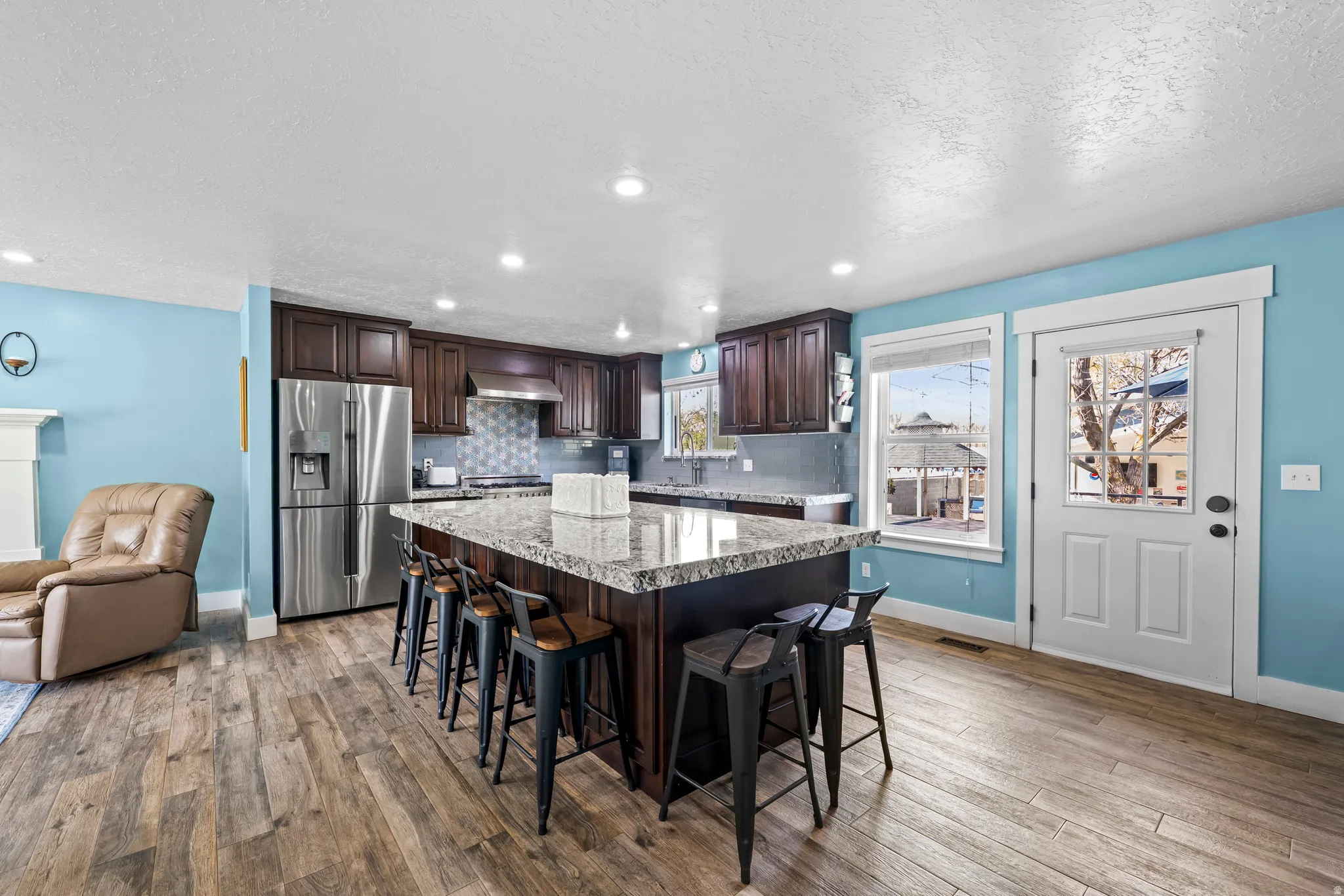 Kitchen featuring dark wood finish cabinetry, a kitchen breakfast bar, a center island, stainless steel refrigerator with ice dispenser, and a textured ceiling