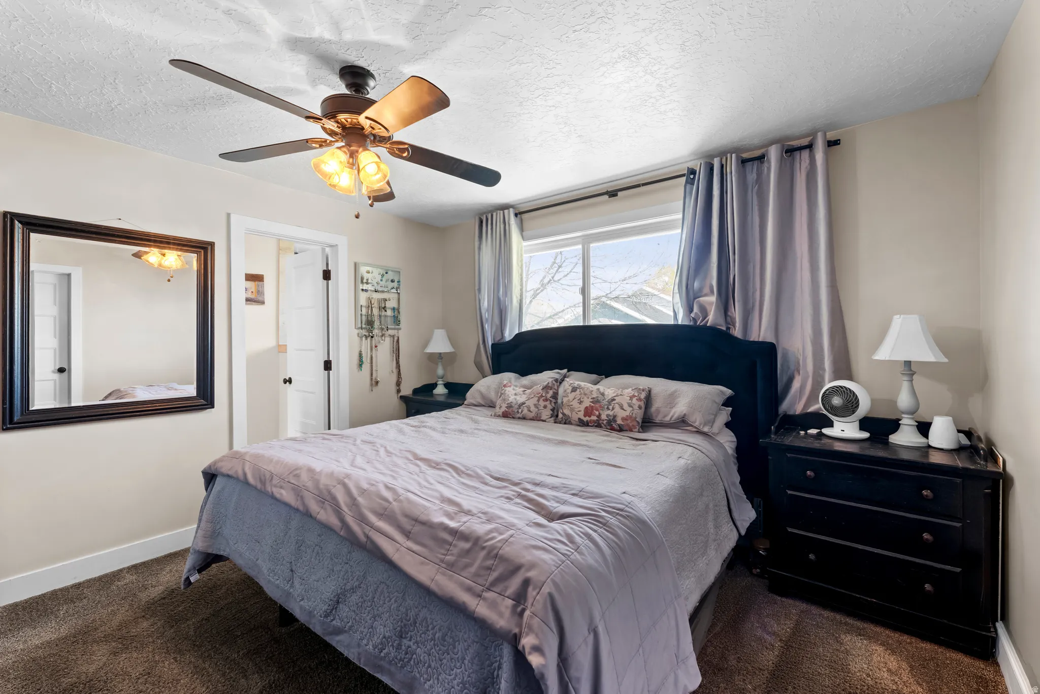 Bedroom with ceiling fan, a textured ceiling, and dark colored carpet