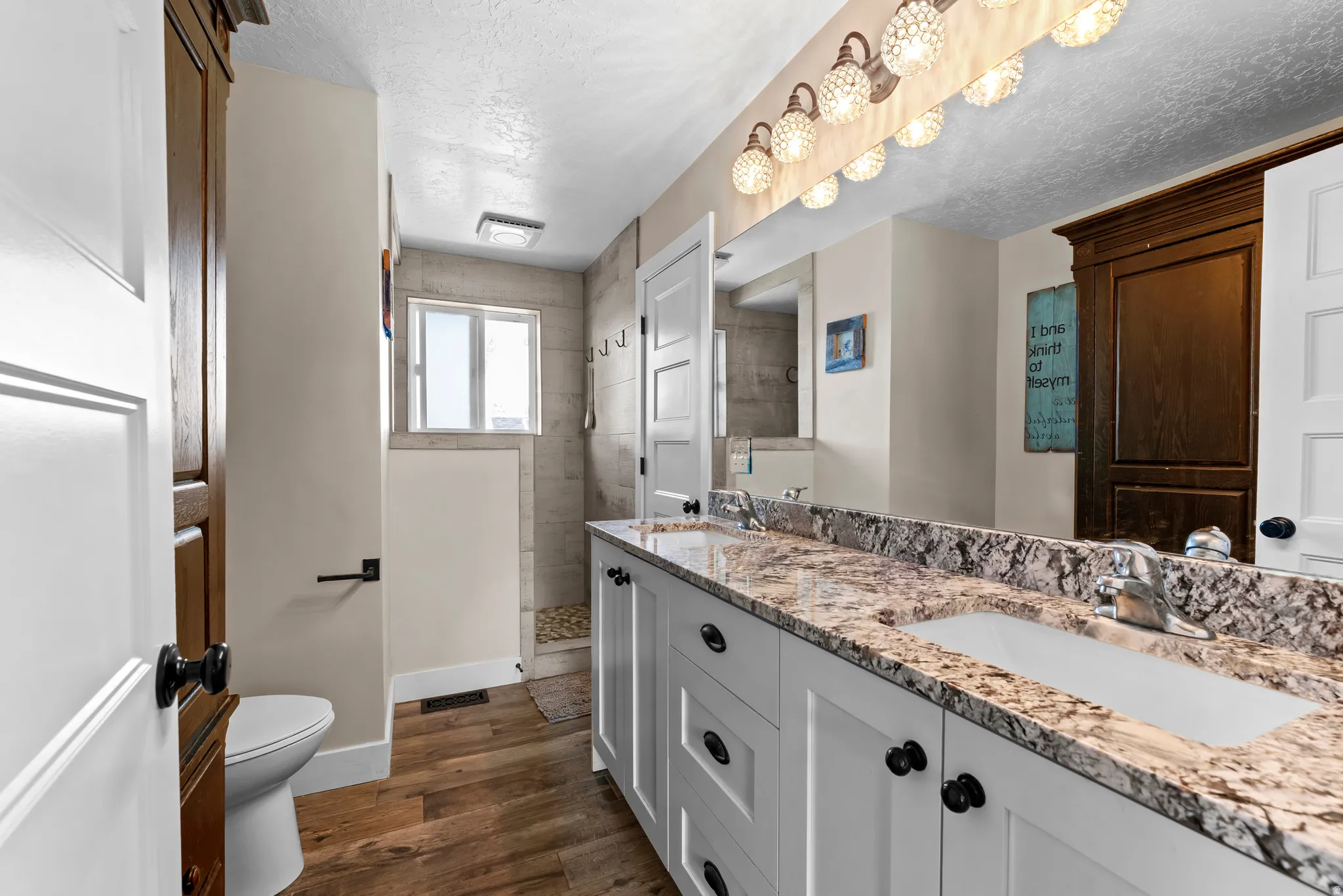 Bathroom with a walk in shower, double vanity, dark wood-style floors, and a textured ceiling