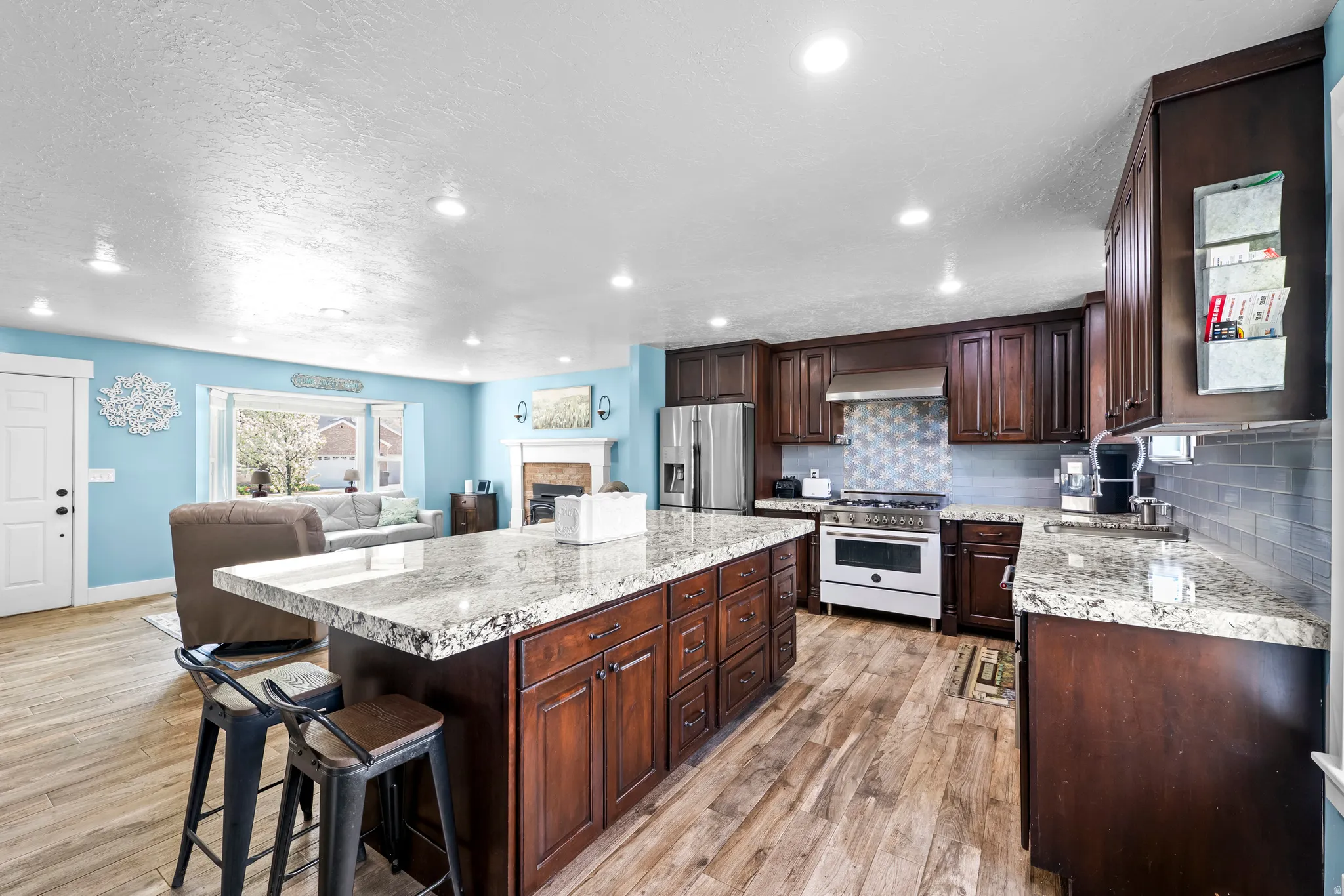 Kitchen featuring range with gas stovetop, open floor plan, light wood-style floors, a fireplace, and dark wood finish cabinets
