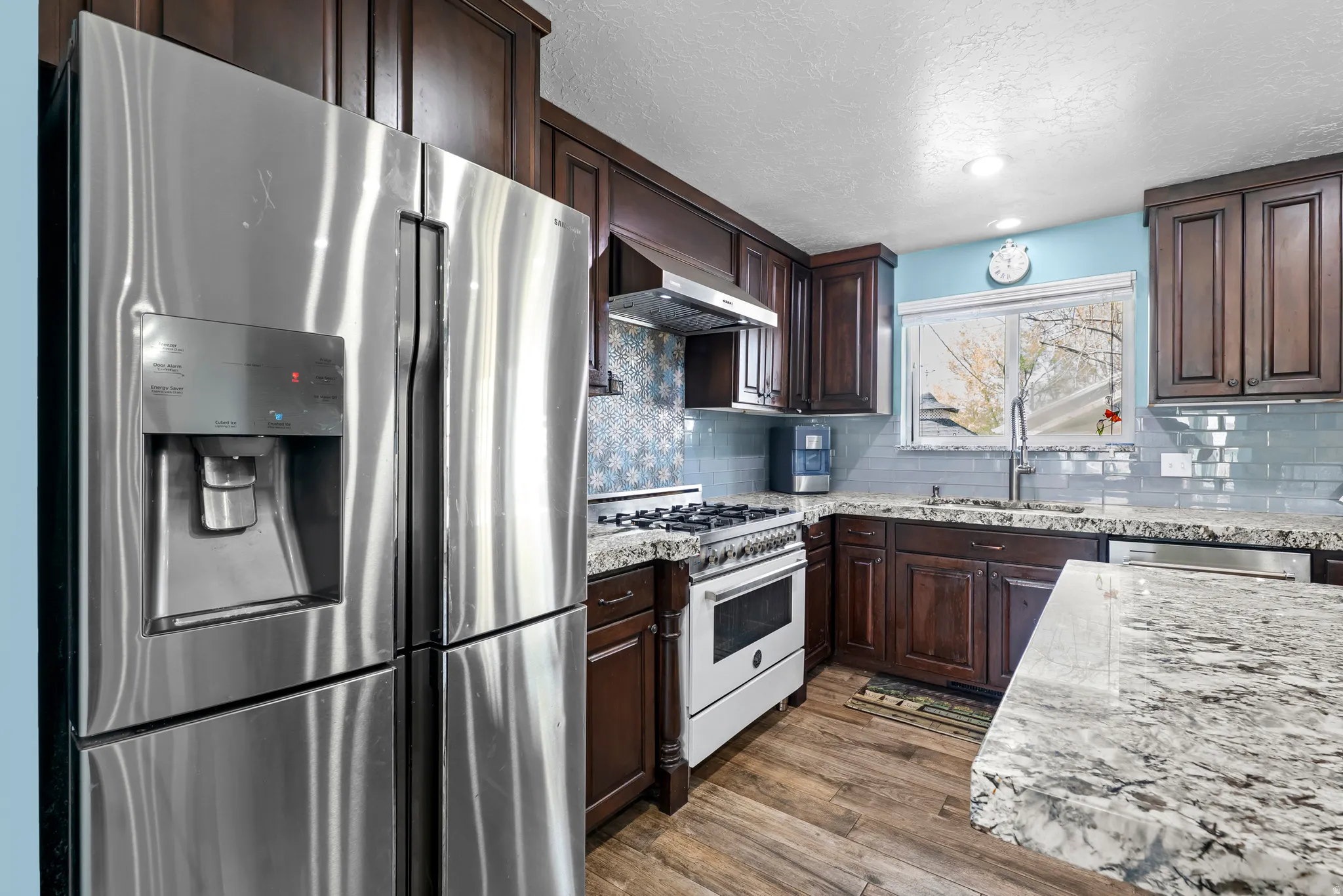 Kitchen with stainless steel appliances, light wood-style floors, dark wood finish cabinets, light stone countertops, and a textured ceiling
