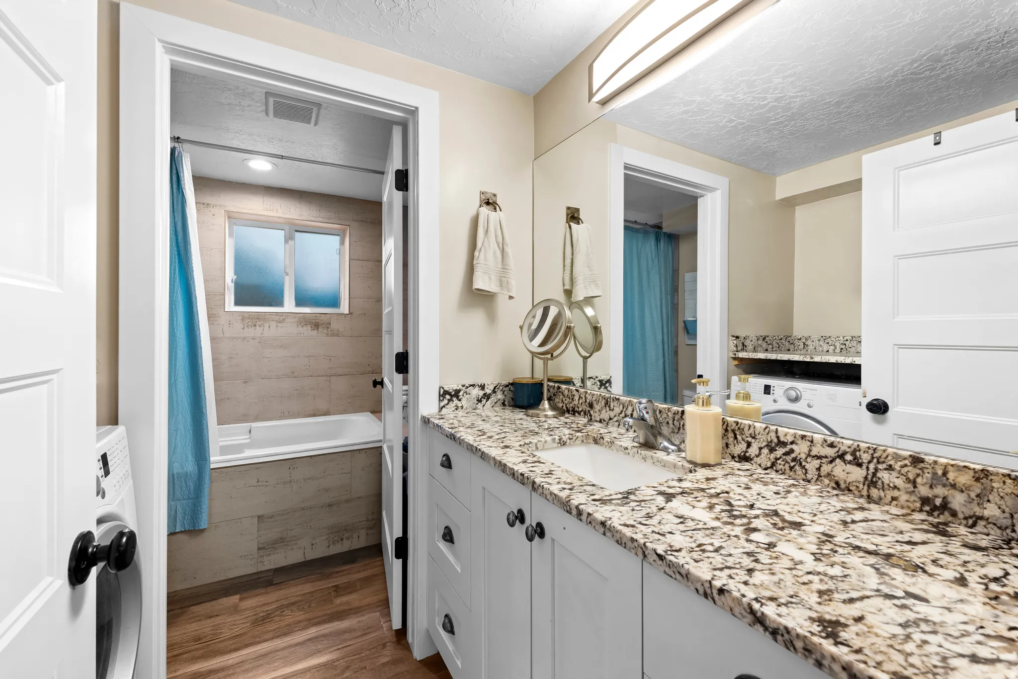 Full bath featuring dark wood-style flooring, vanity, washer / dryer, a textured ceiling, and tiled shower / bath