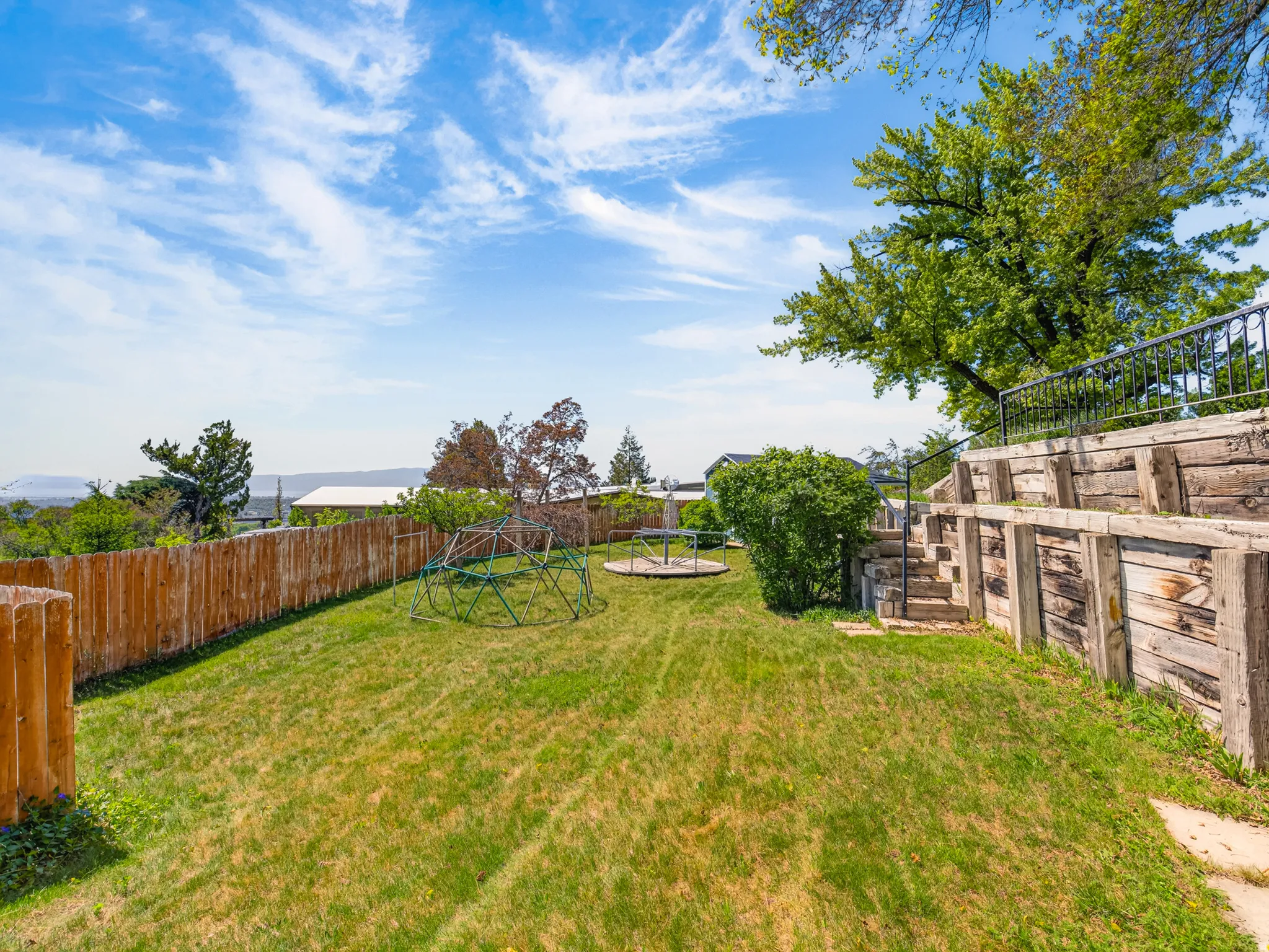 Expansive backyard featuring a manicured lawn, a wood fence, and a multi-tiered retaining wall with steps