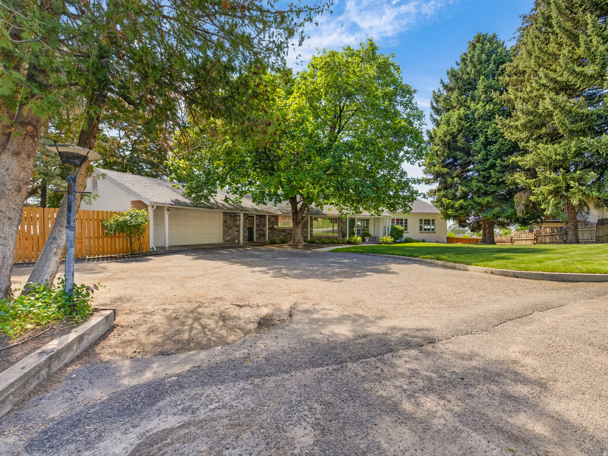 Spacious asphalt driveway with an attached garage, natural wood fencing, and mature trees providing shade
