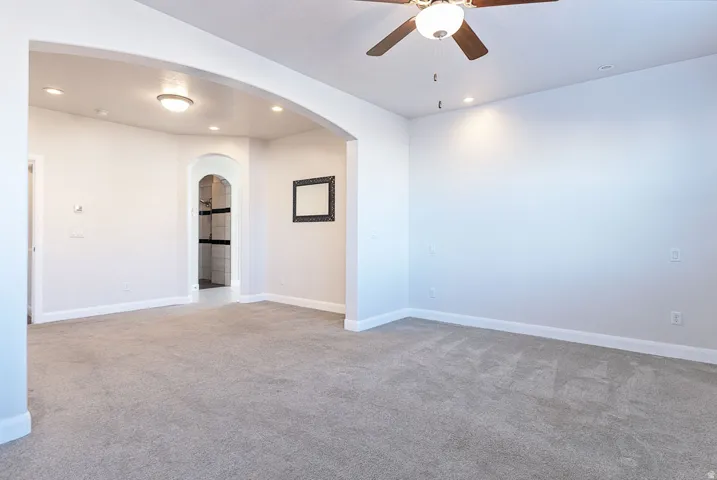 Empty room featuring ceiling fan, light colored carpet, recessed lighting, and arched walkways