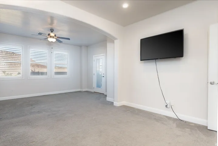 Unfurnished living room featuring ceiling fan, arched walkways, and light carpet