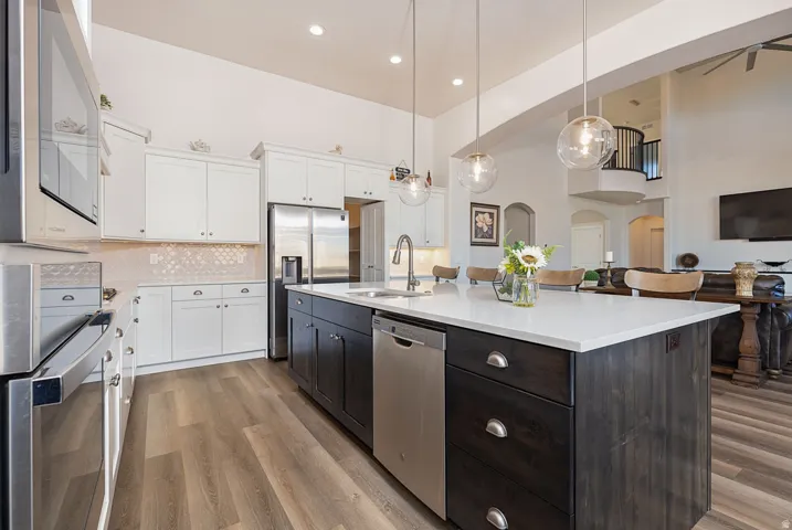 Kitchen with two tone cabinetry, a high ceiling, a center island with sink, stainless steel appliances, and decorative backsplash