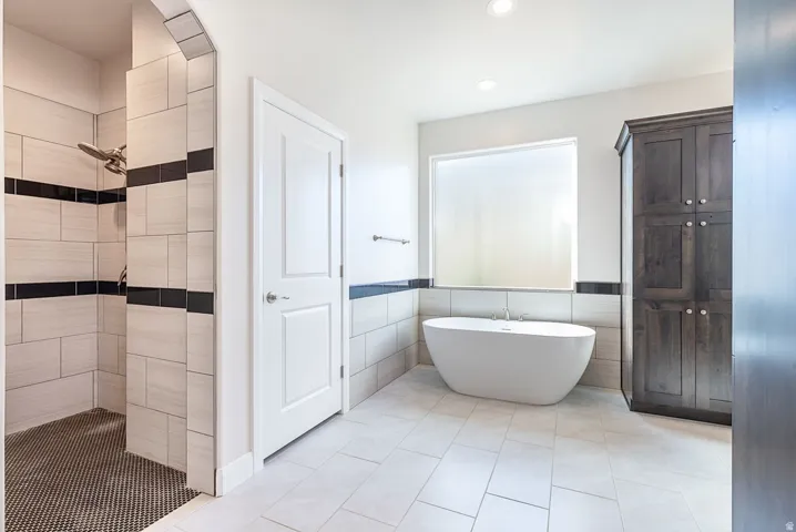Full bath featuring a shower stall, a freestanding bath, tile walls, light tile patterned floors, and a wainscoted wall