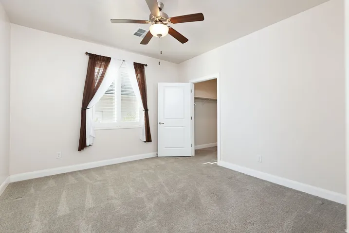 Unfurnished bedroom with a walk in closet, light colored carpet, and ceiling fan