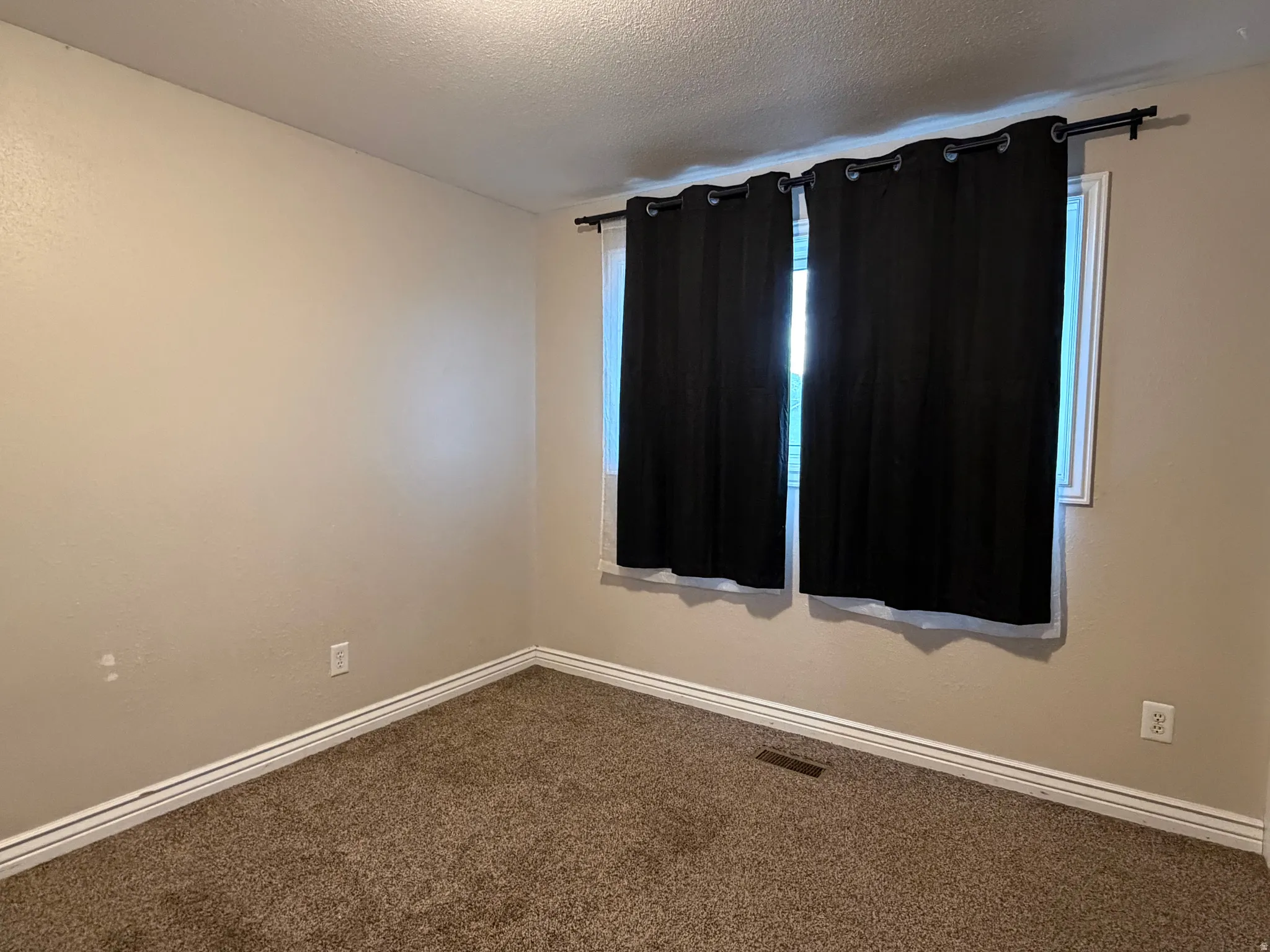 Unfurnished room with a textured ceiling and dark colored carpet