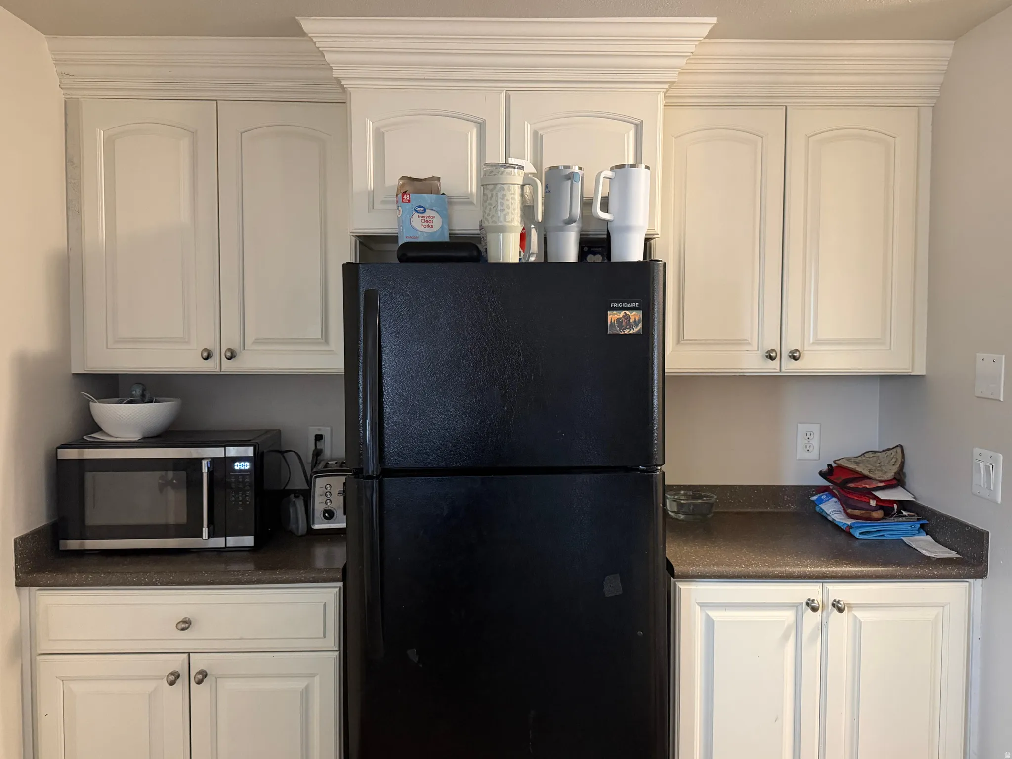 Kitchen featuring dark countertops, freestanding refrigerator, stainless steel microwave, and white cabinetry