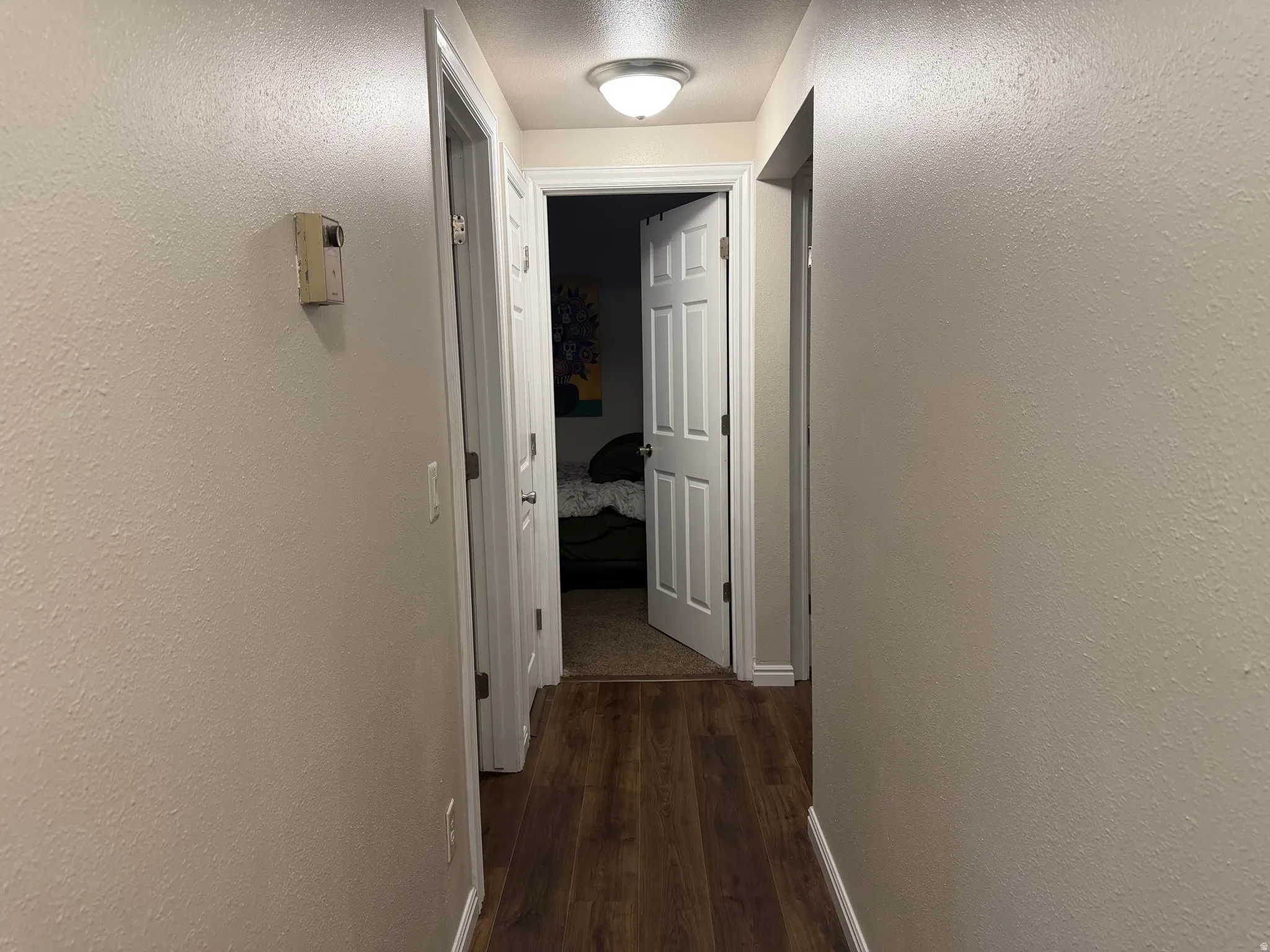Corridor with a textured wall, dark wood-style flooring, and a textured ceiling