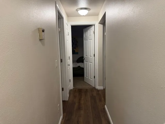 Corridor with a textured wall, dark wood-style flooring, and a textured ceiling