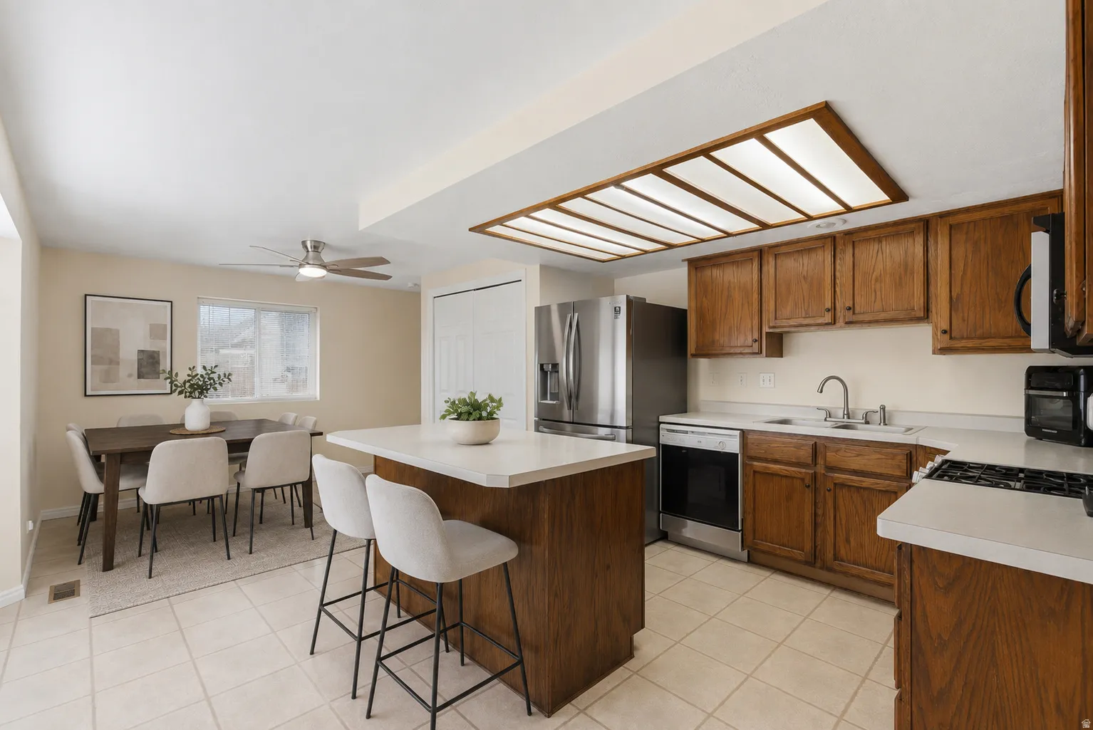 Virtually Staged - Kitchen with wood-finish cabinetry and light countertops, featuring a new stainless steel refrigerator (new in the box) and dishwasher -Staged