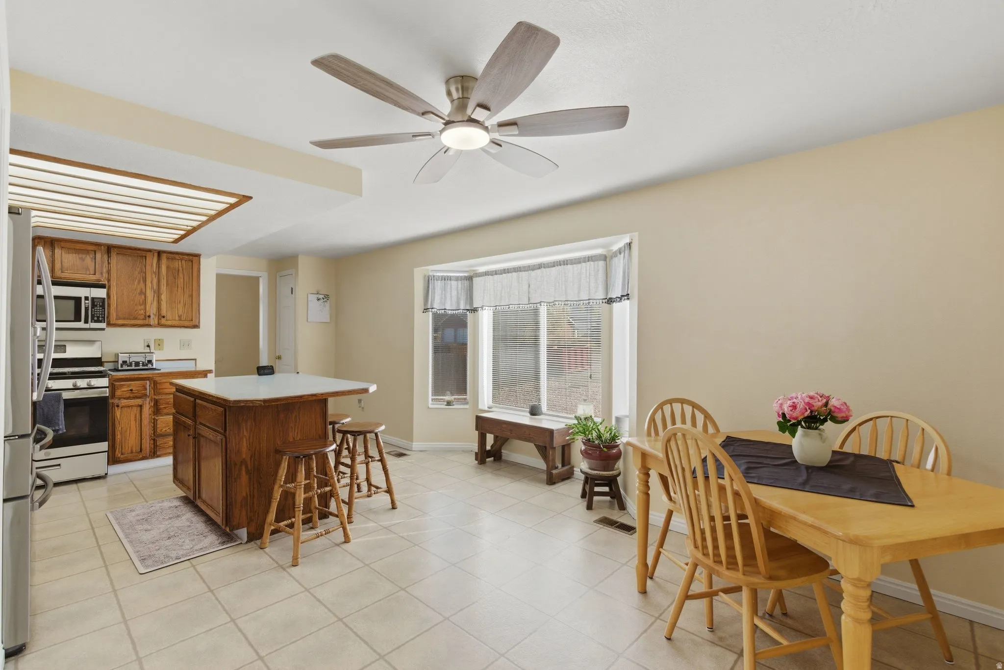 Kitchen with wood finish cabinetry, stainless steel appliances, light countertops, a breakfast bar area, and a ceiling fan