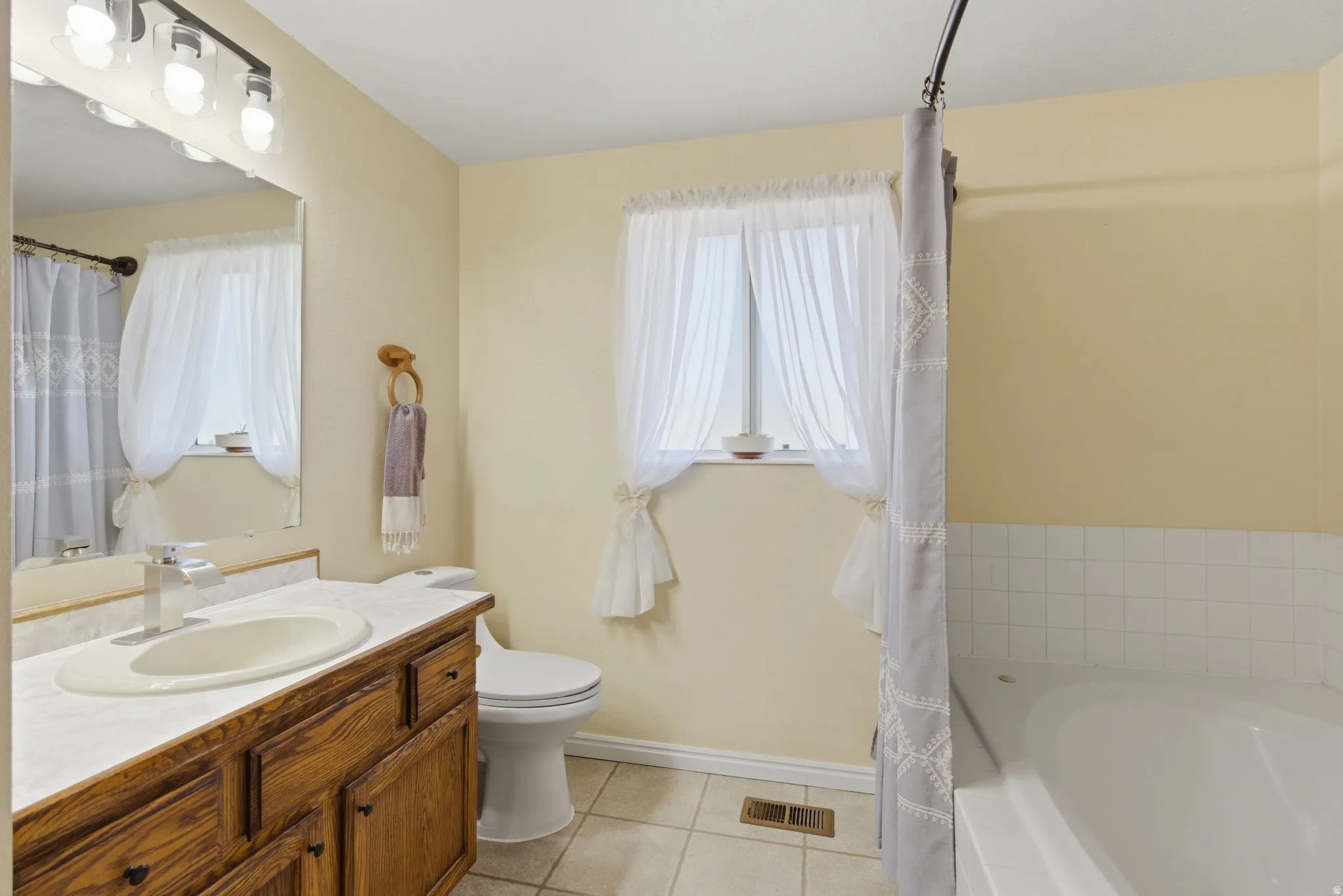 Bathroom with vanity, light tile patterned floors, a bath, and a shower with a shower curtain.