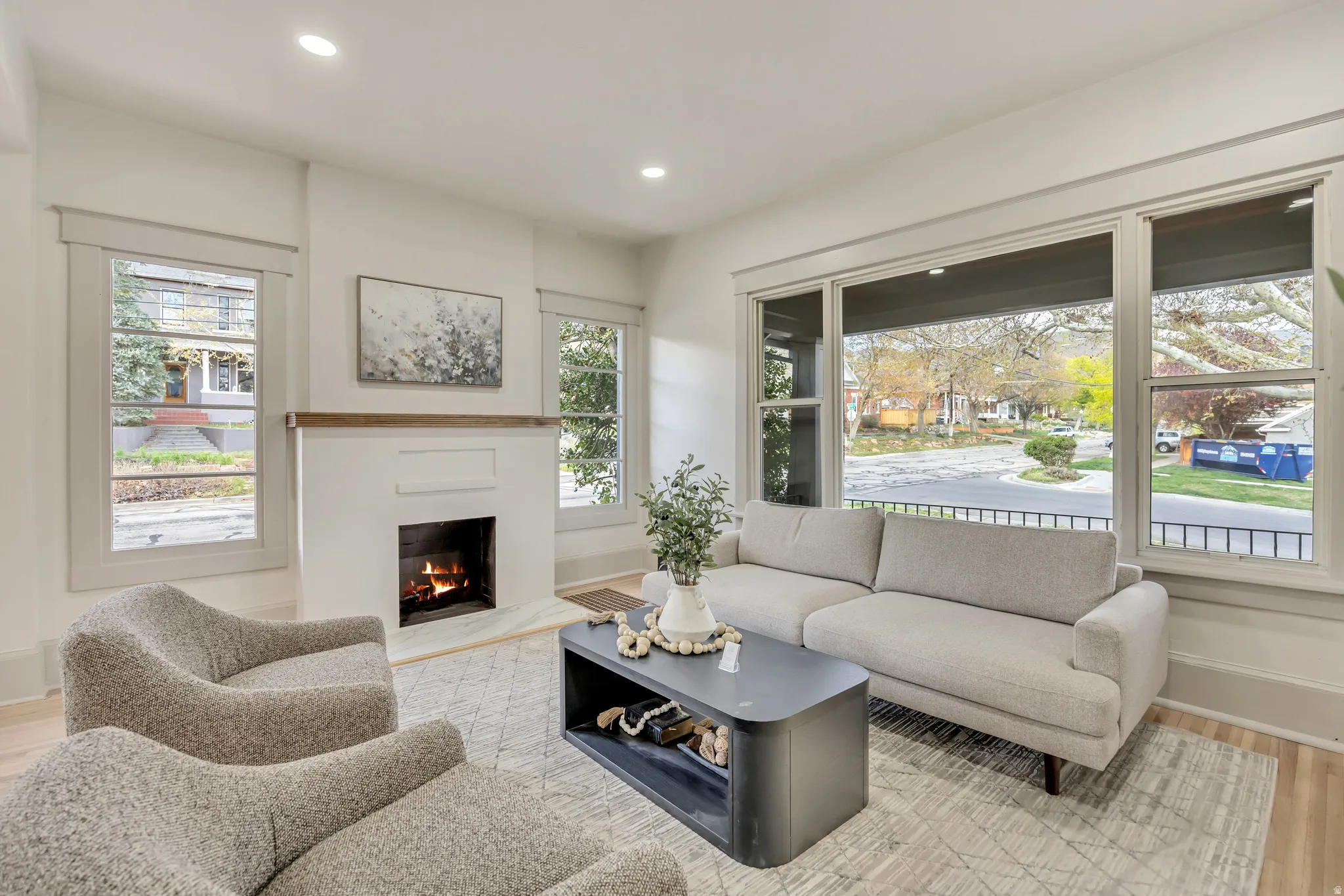 Living room with light wood finished floors, a warm lit fireplace, and recessed lighting