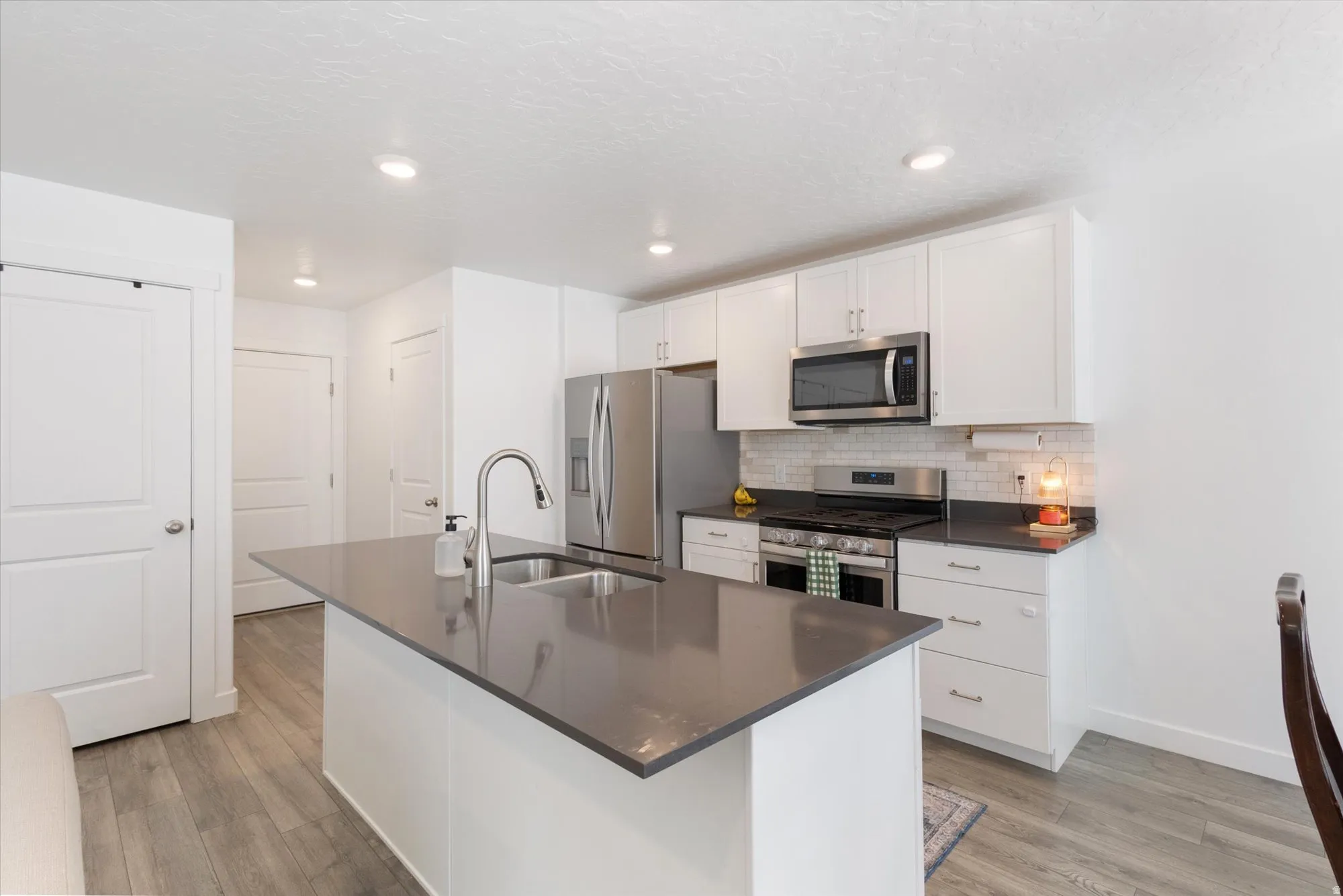 Kitchen featuring stainless steel appliances, white cabinetry, light wood-style floors, a kitchen island with sink, and decorative backsplash