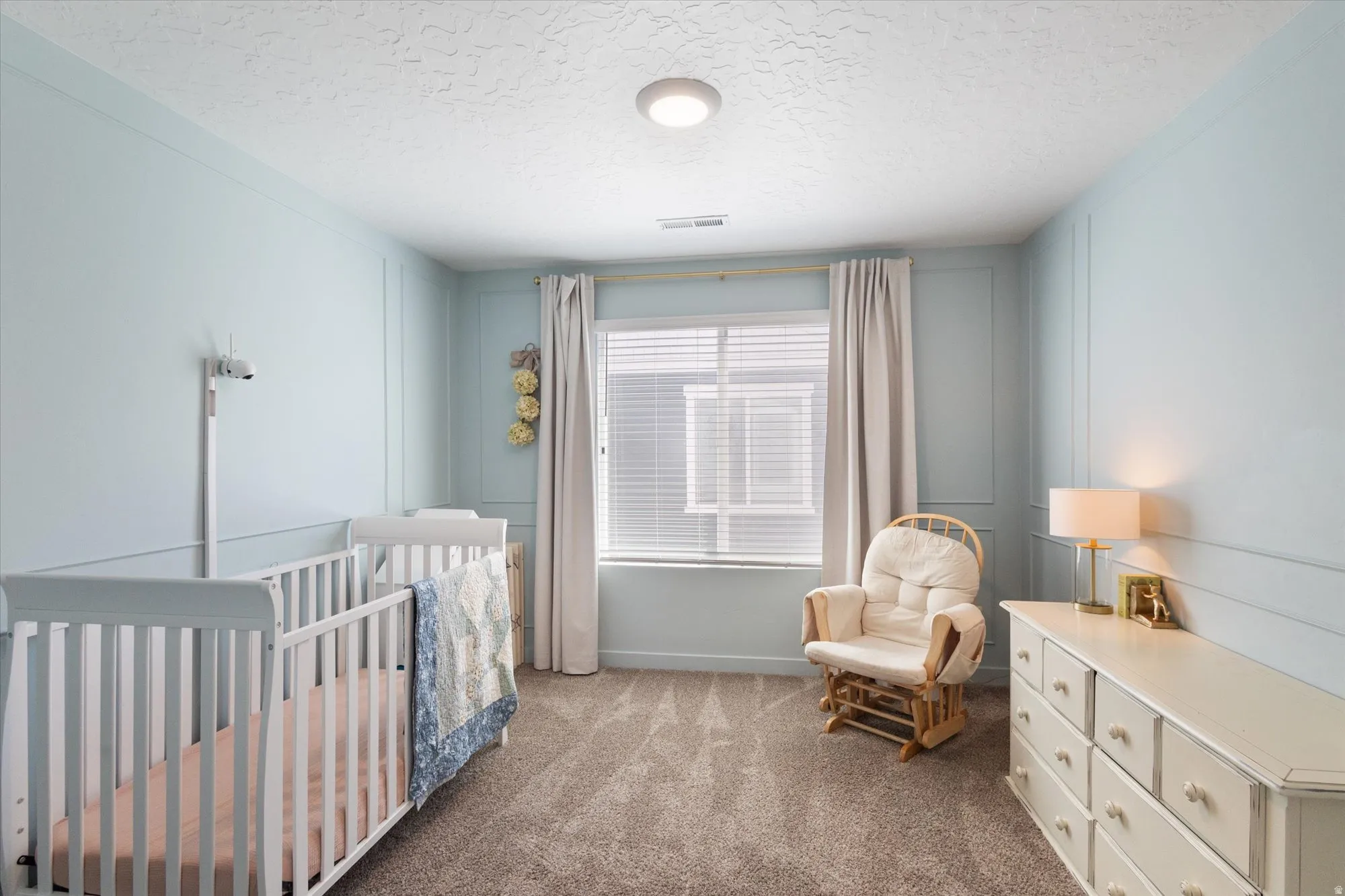 Bedroom with a crib, carpet, and a textured ceiling