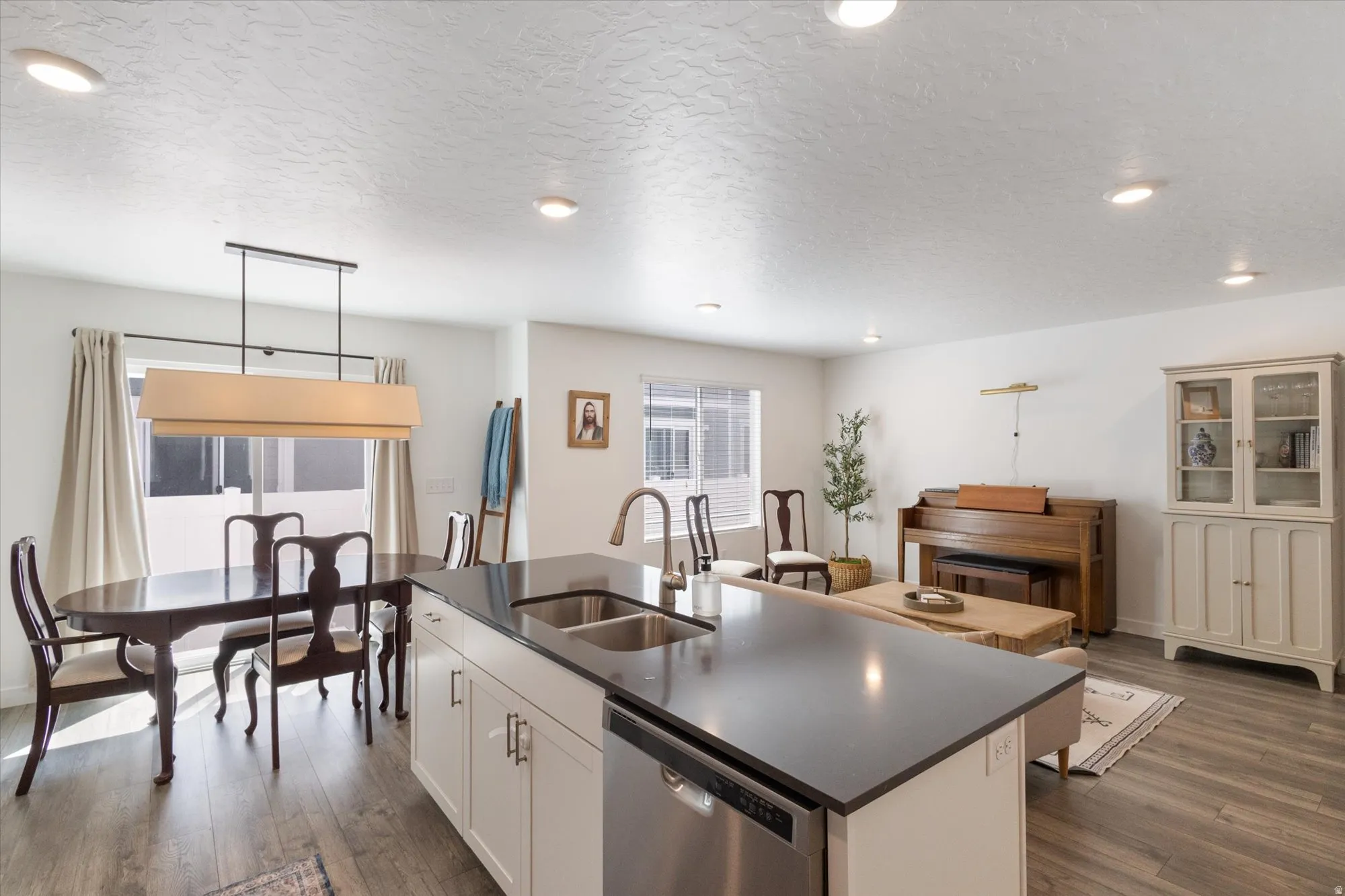 Kitchen with a kitchen island with sink, dishwasher, white cabinetry, pendant lighting, and a textured ceiling