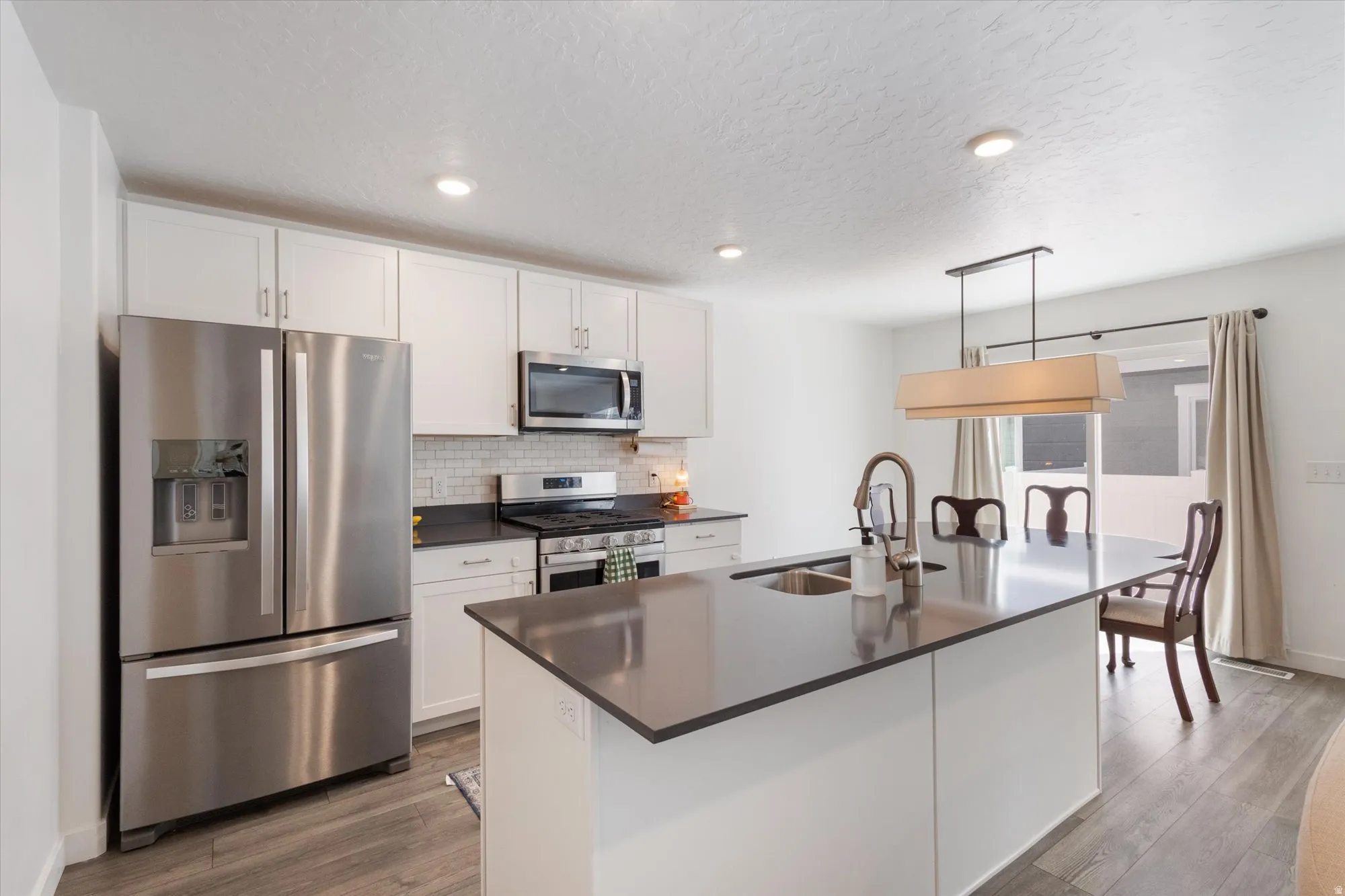 Kitchen featuring stainless steel appliances, white cabinets, decorative light fixtures, light wood-style floors, and tasteful backsplash