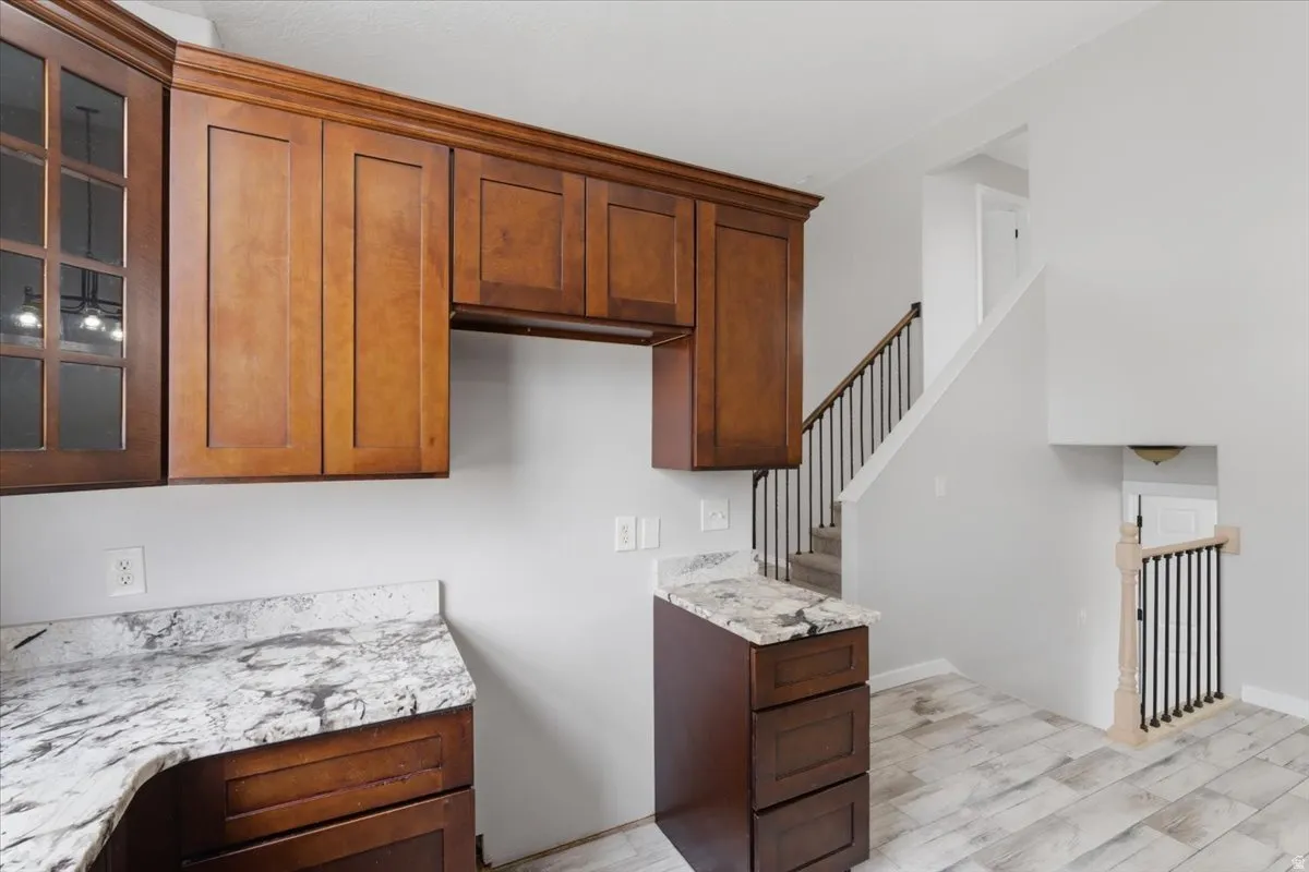 Kitchen featuring glass fronted cabinets, light wood-type flooring, light stone counters, and wood finish cabinetry