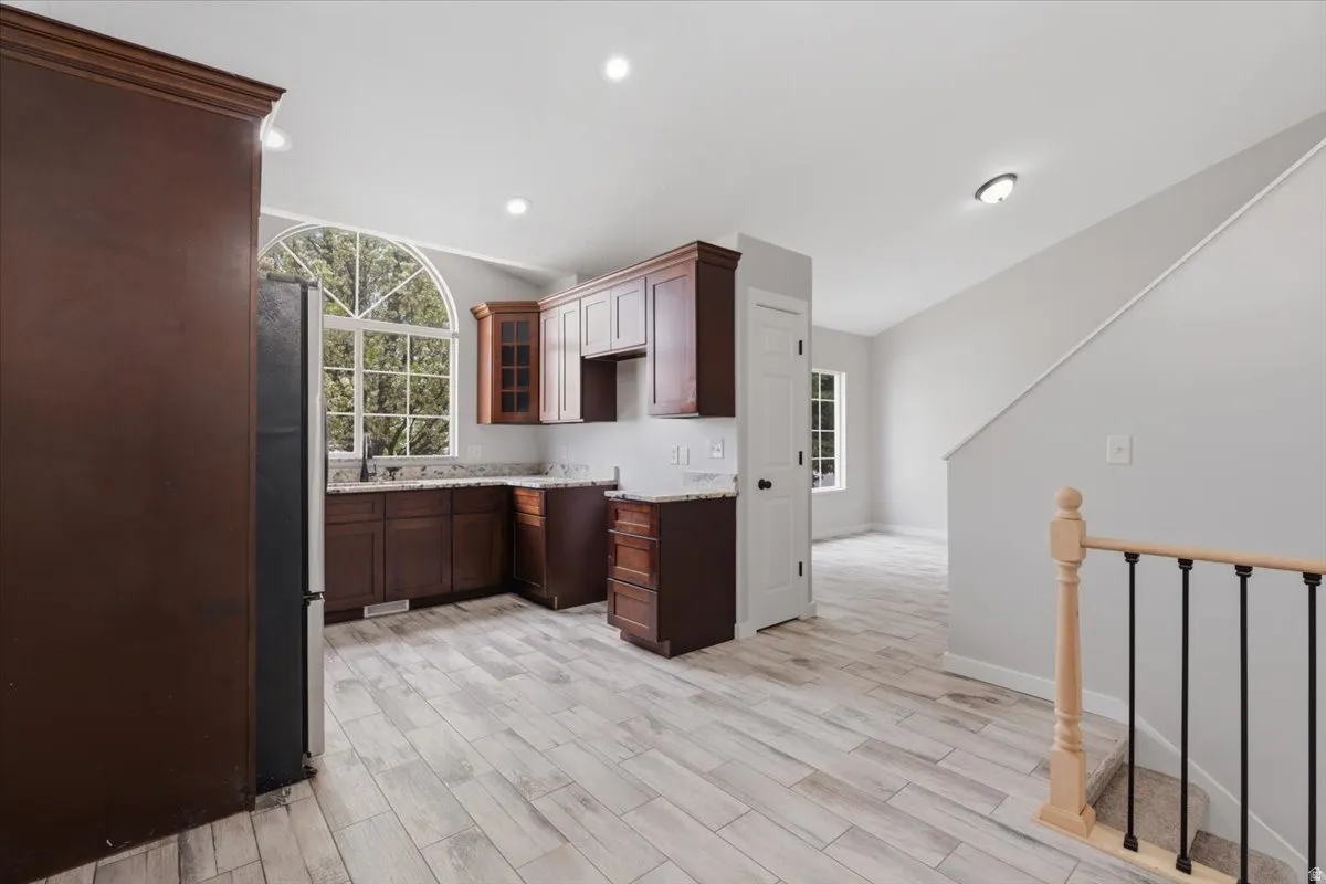 Kitchen with wood tiled floors, freestanding refrigerator, recessed lighting, dark wood finish cabinets, and glass insert cabinets