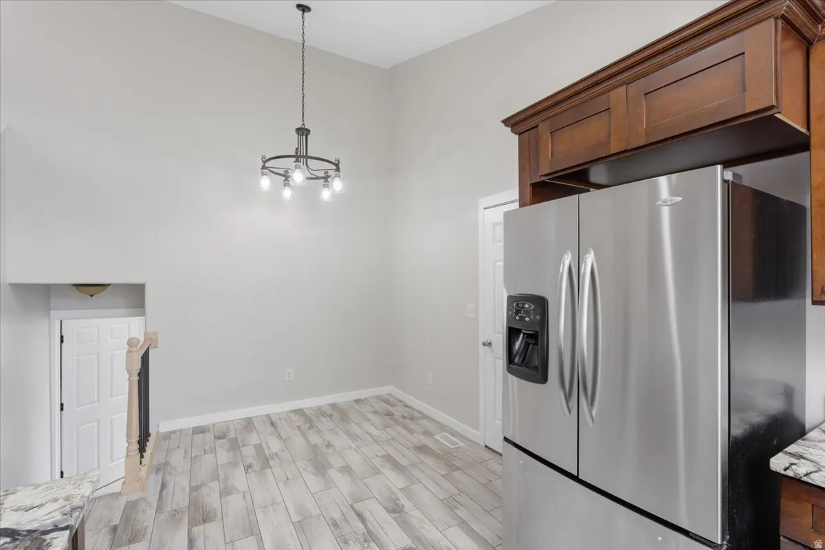 Kitchen with stainless steel fridge, wood finish floors, light stone countertops, a high ceiling, and hanging lights