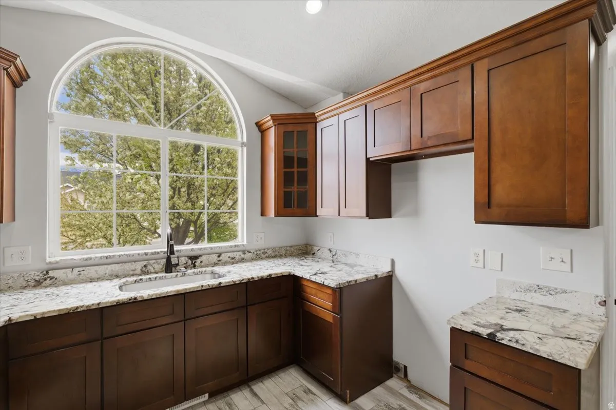 Kitchen with glass insert cabinets, light stone countertops, light wood finished floors, and lofted ceiling