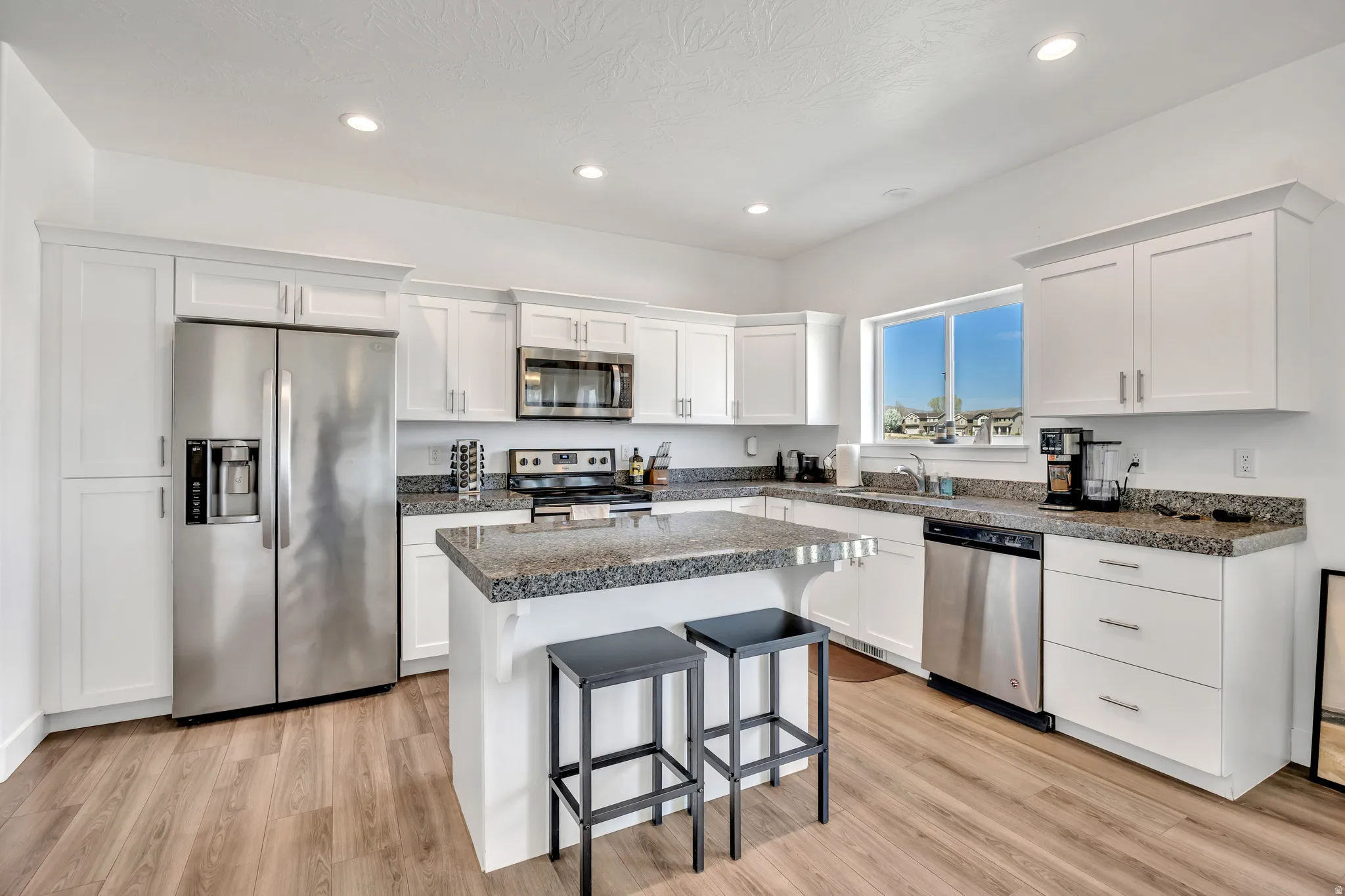 Kitchen with stainless steel appliances, a breakfast bar, white cabinetry, a kitchen island, and recessed lighting