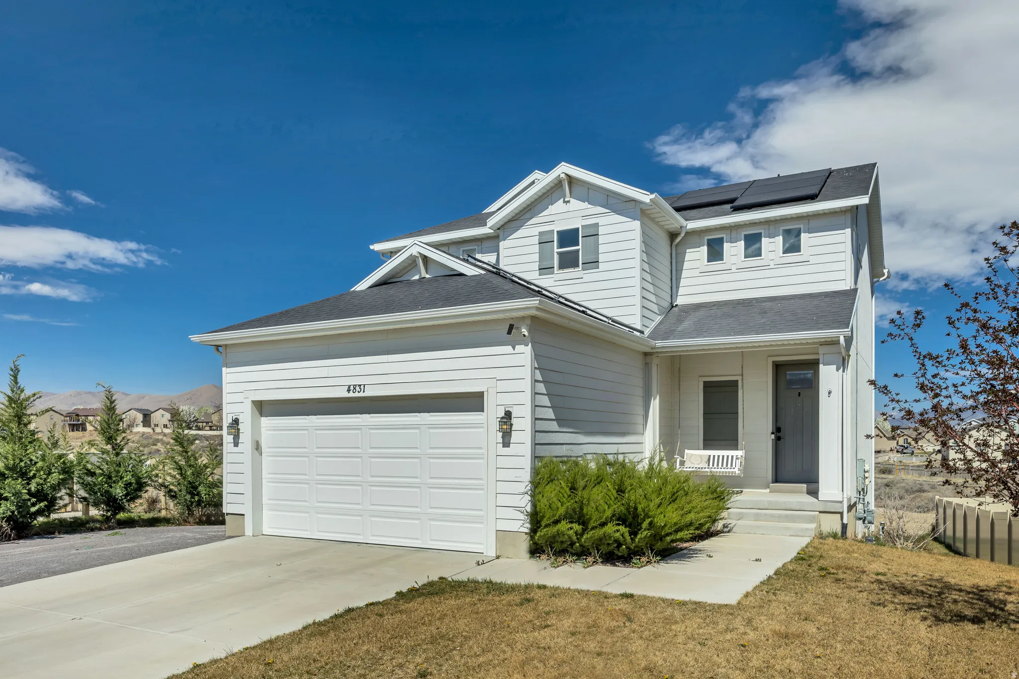 View of front of house with roof mounted solar panels, covered porch, concrete driveway, a garage, and a front lawn