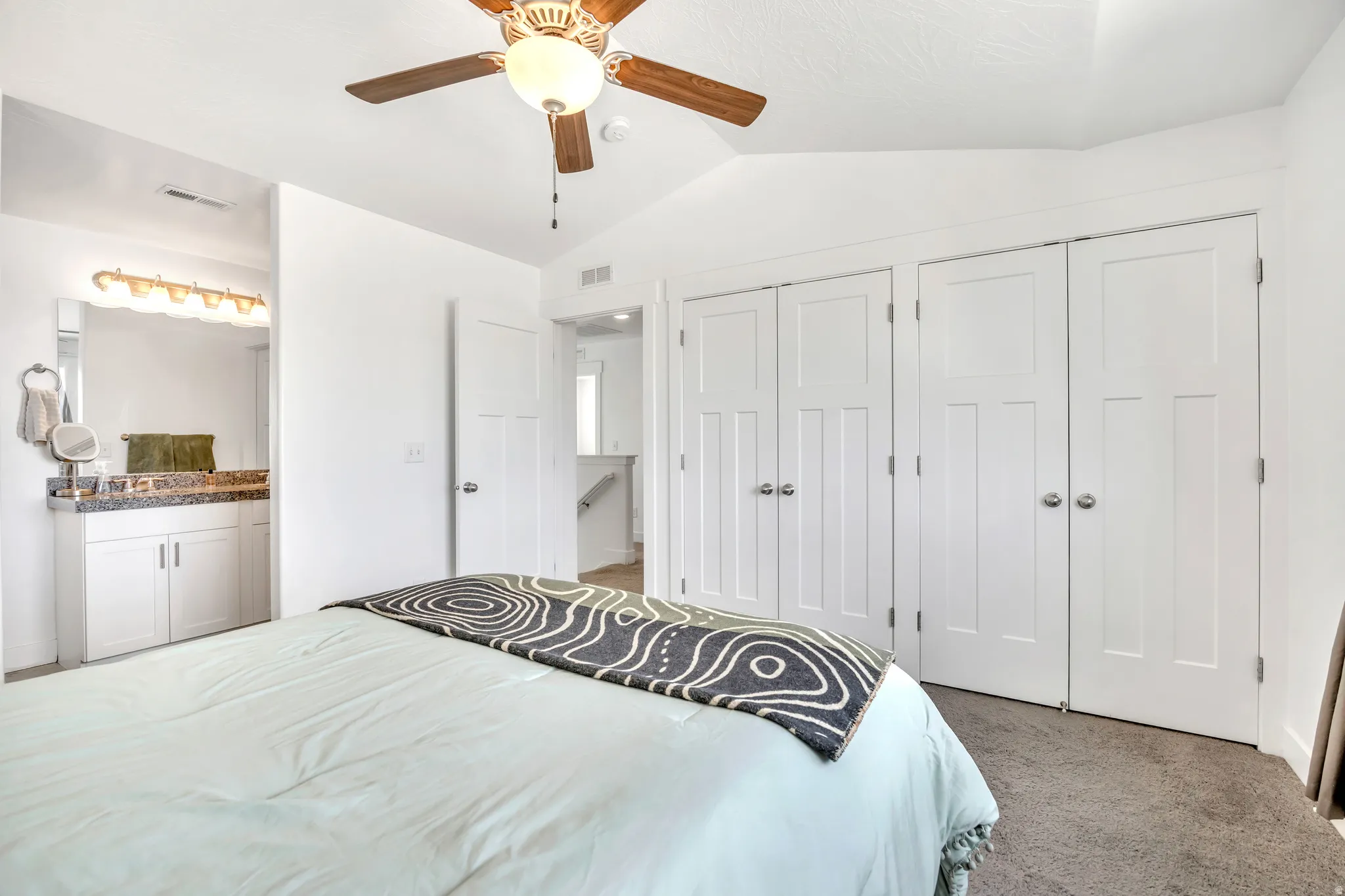 Carpeted bedroom featuring vaulted ceiling, a closet, a ceiling fan, and ensuite bath