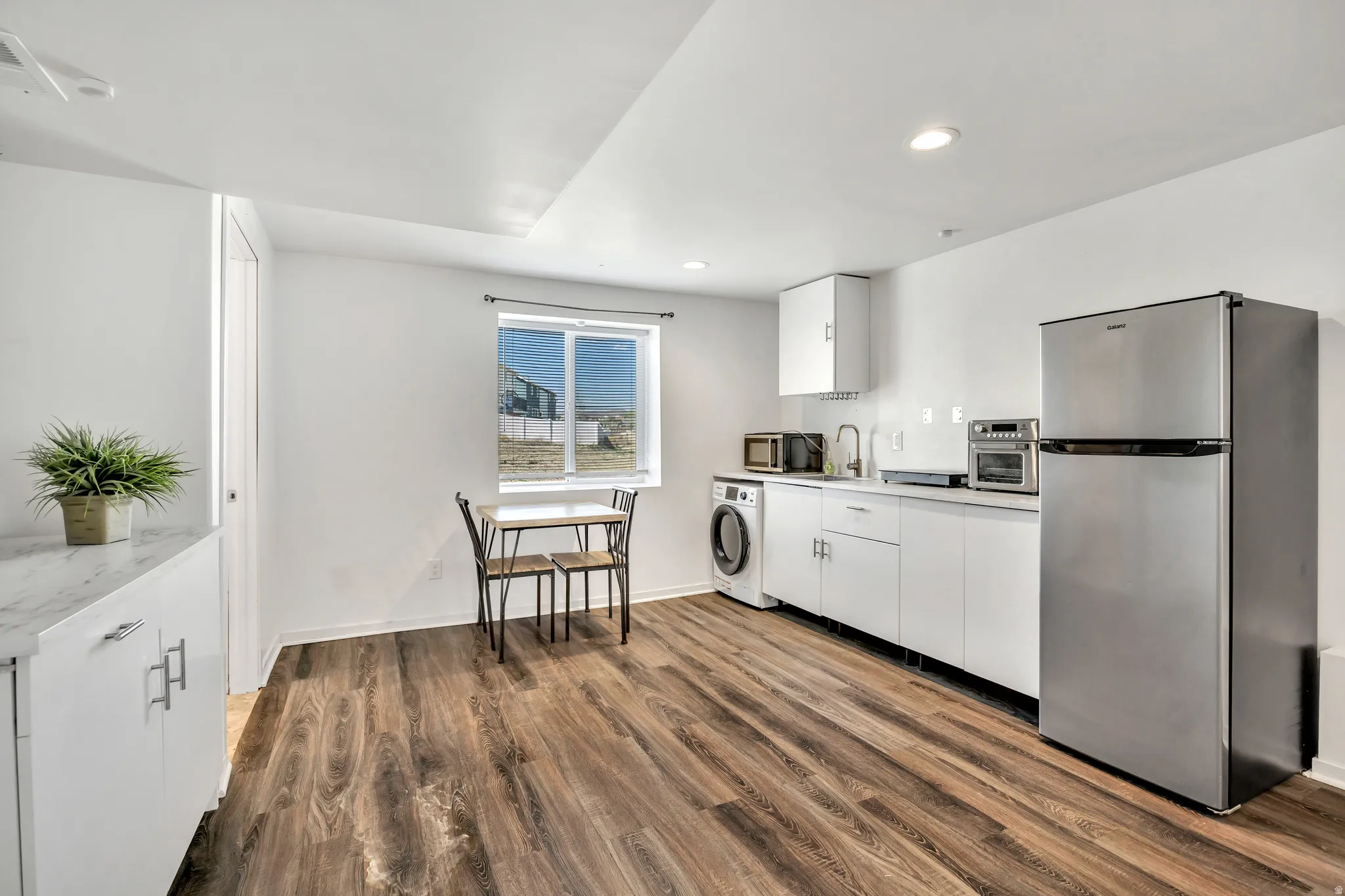 Kitchen featuring stainless steel appliances, white cabinetry, light countertops, dark wood-type flooring, and recessed lighting