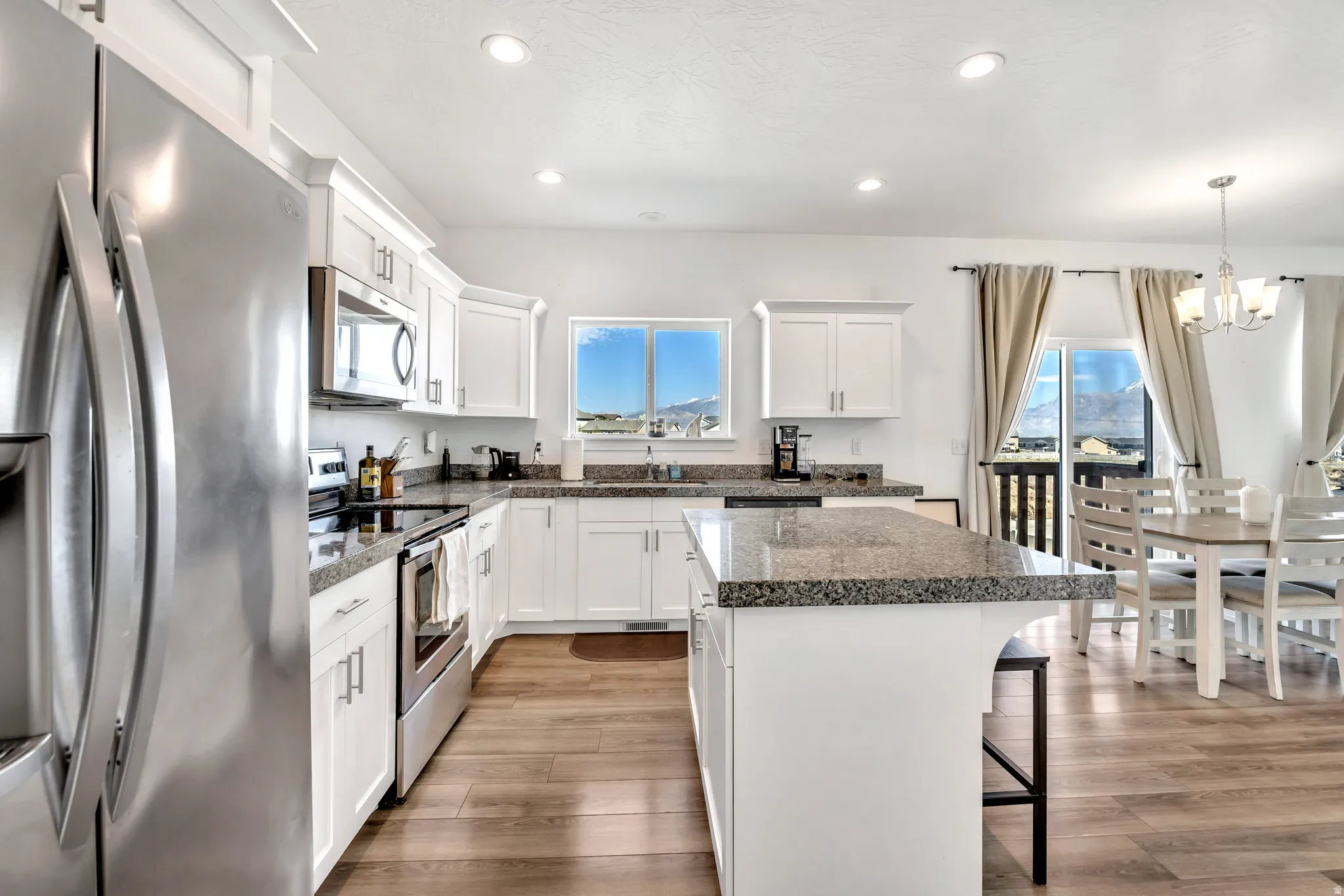 Kitchen with stainless steel appliances, suspended lighting, white cabinetry, a breakfast bar, and light wood finished floors