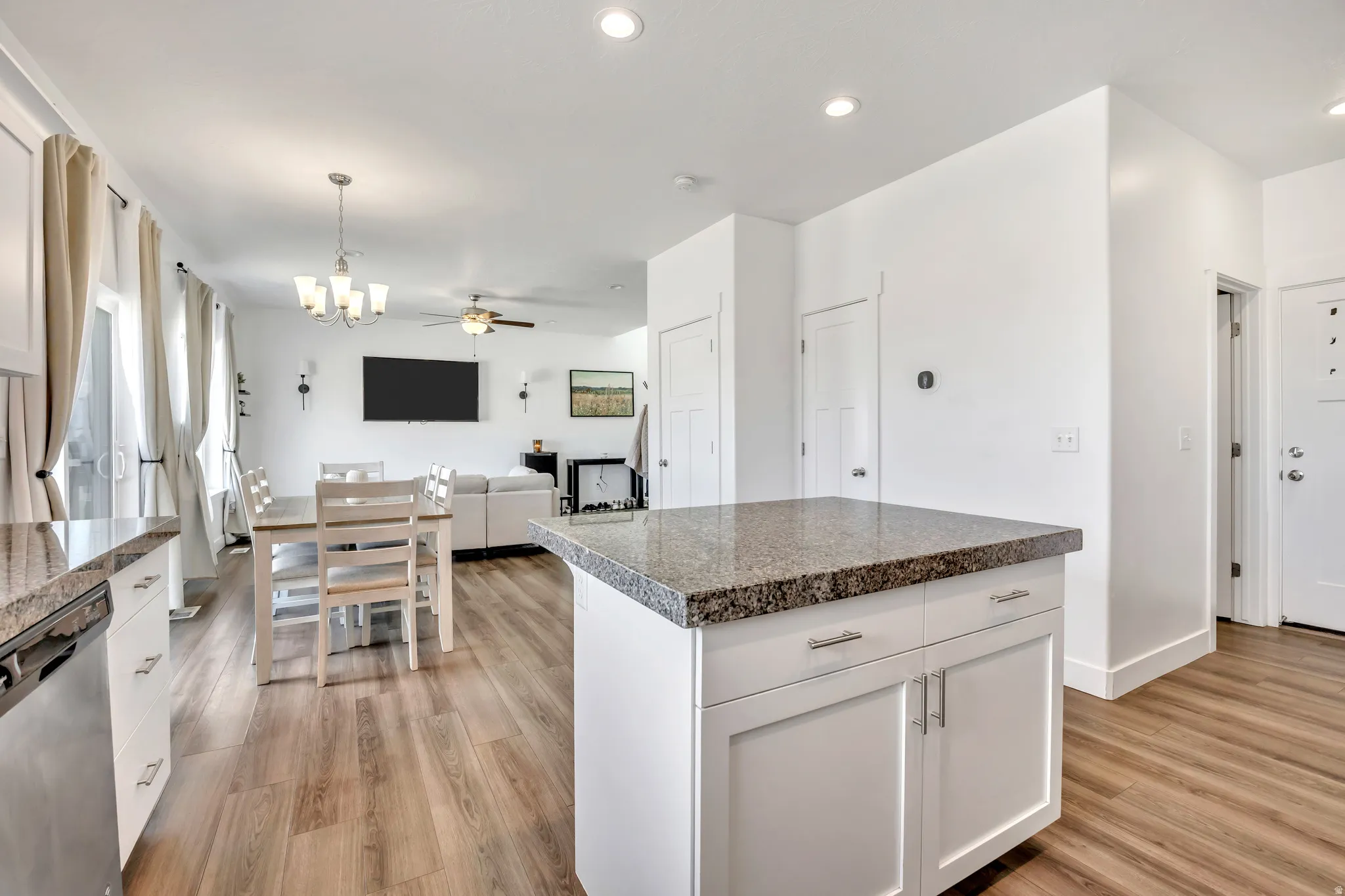 Kitchen featuring dishwasher, open floor plan, white cabinets, hanging lights, and a kitchen island