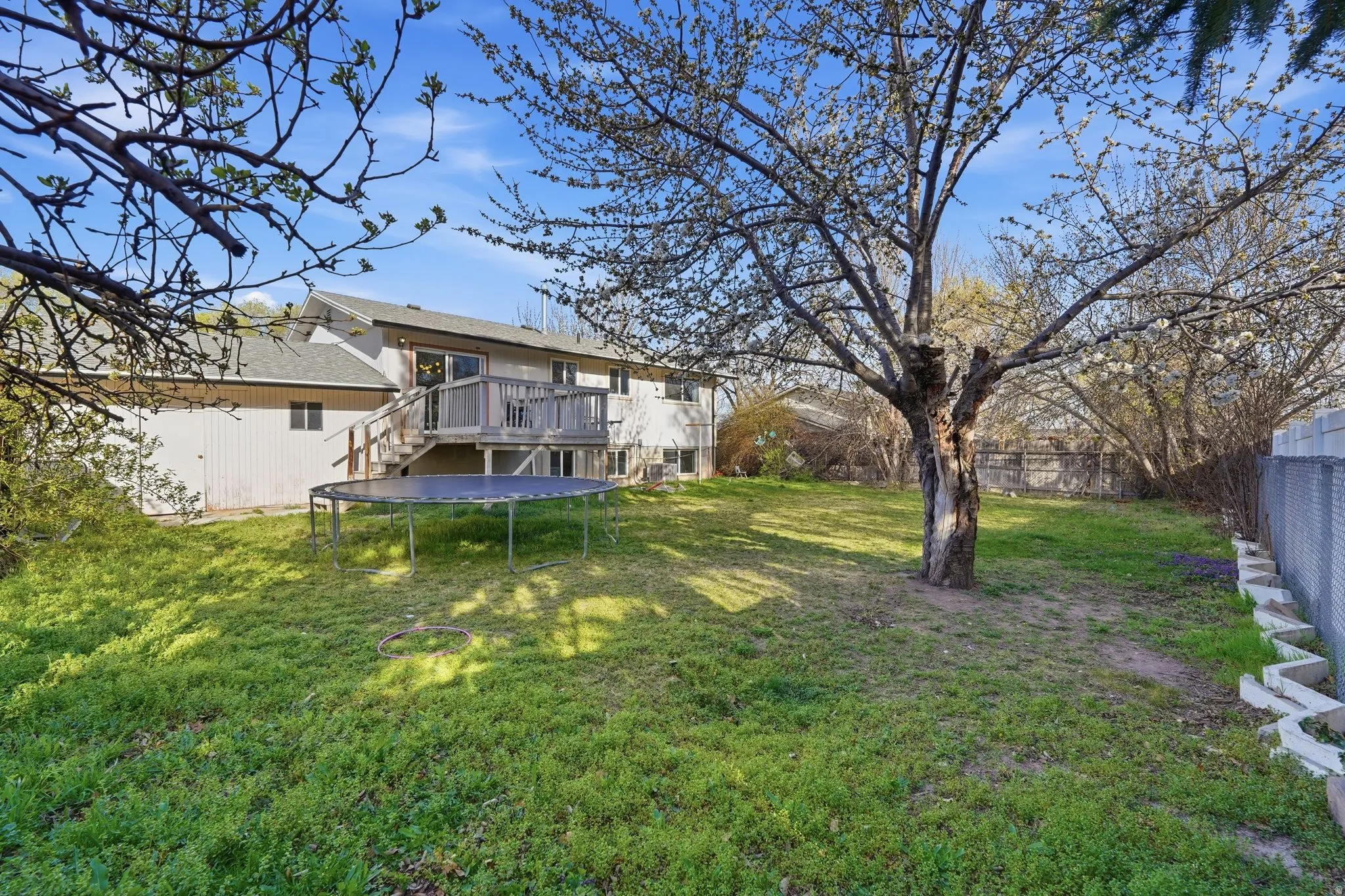 Rear view of house with a deck, a fenced backyard, and a trampoline