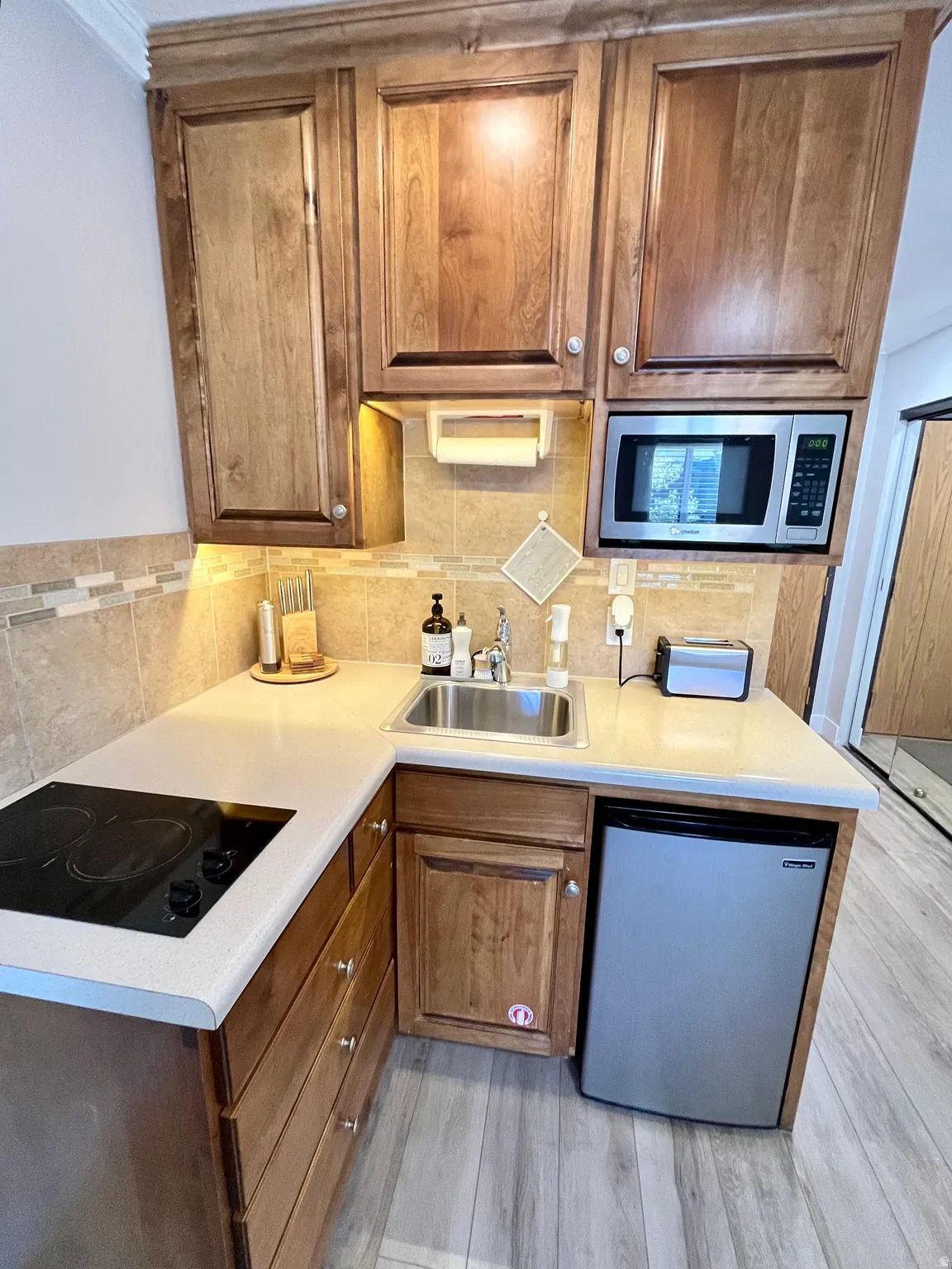 Kitchen featuring stainless steel appliances, light countertops, wood finish cabinetry, light wood-type flooring, and decorative backsplash