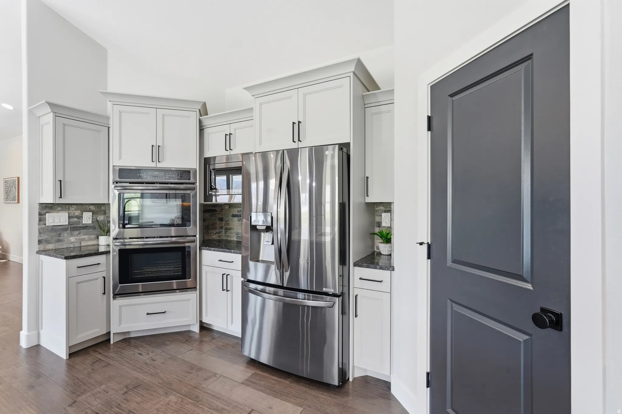 Kitchen featuring stainless steel appliances, double wall oven, hardwood floors, dark granite counters, white cabinetry, and vaulted ceiling