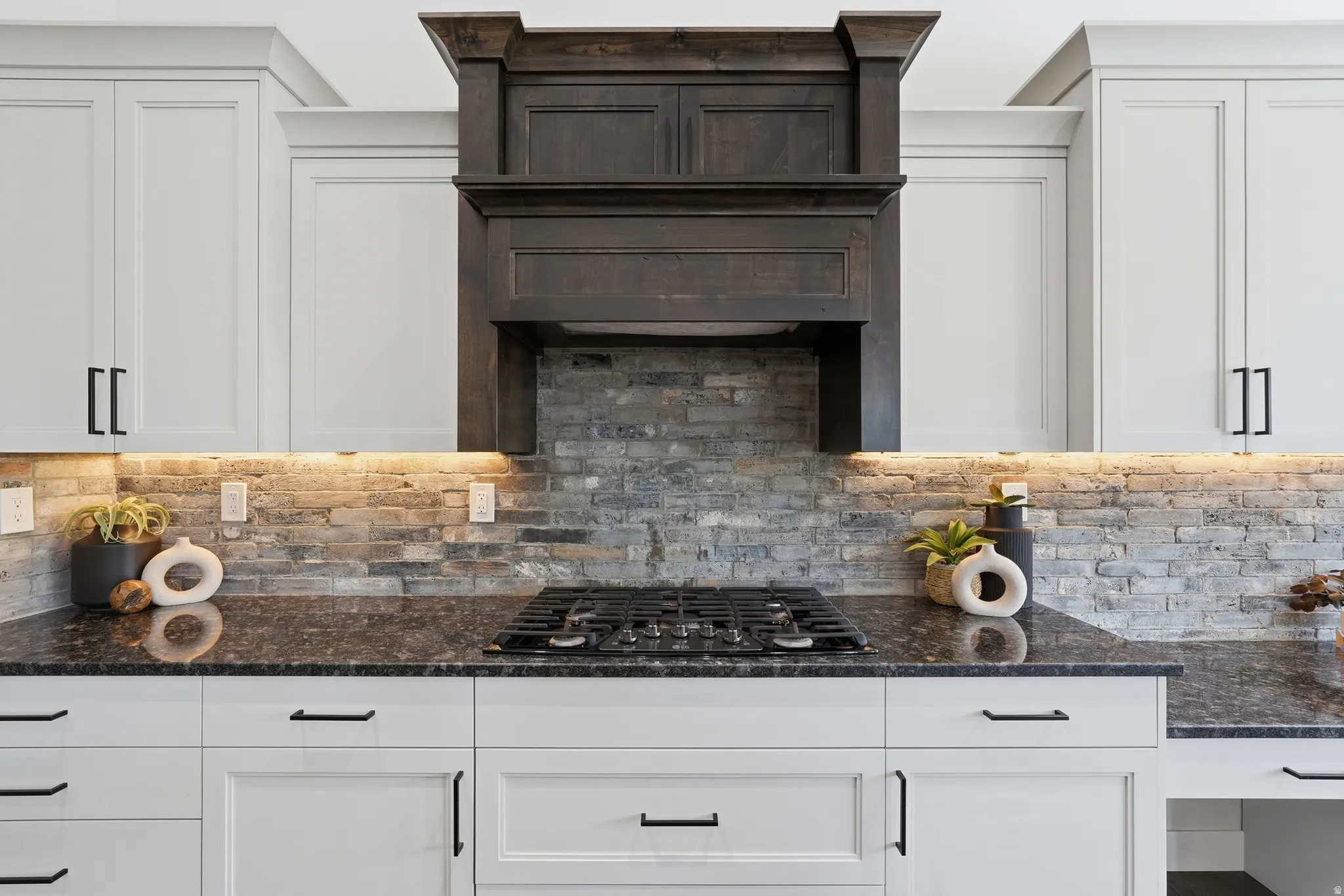 Kitchen featuring dark granite countertops, gas stovetop, white cabinets, ventilation hood, and decorative backsplash