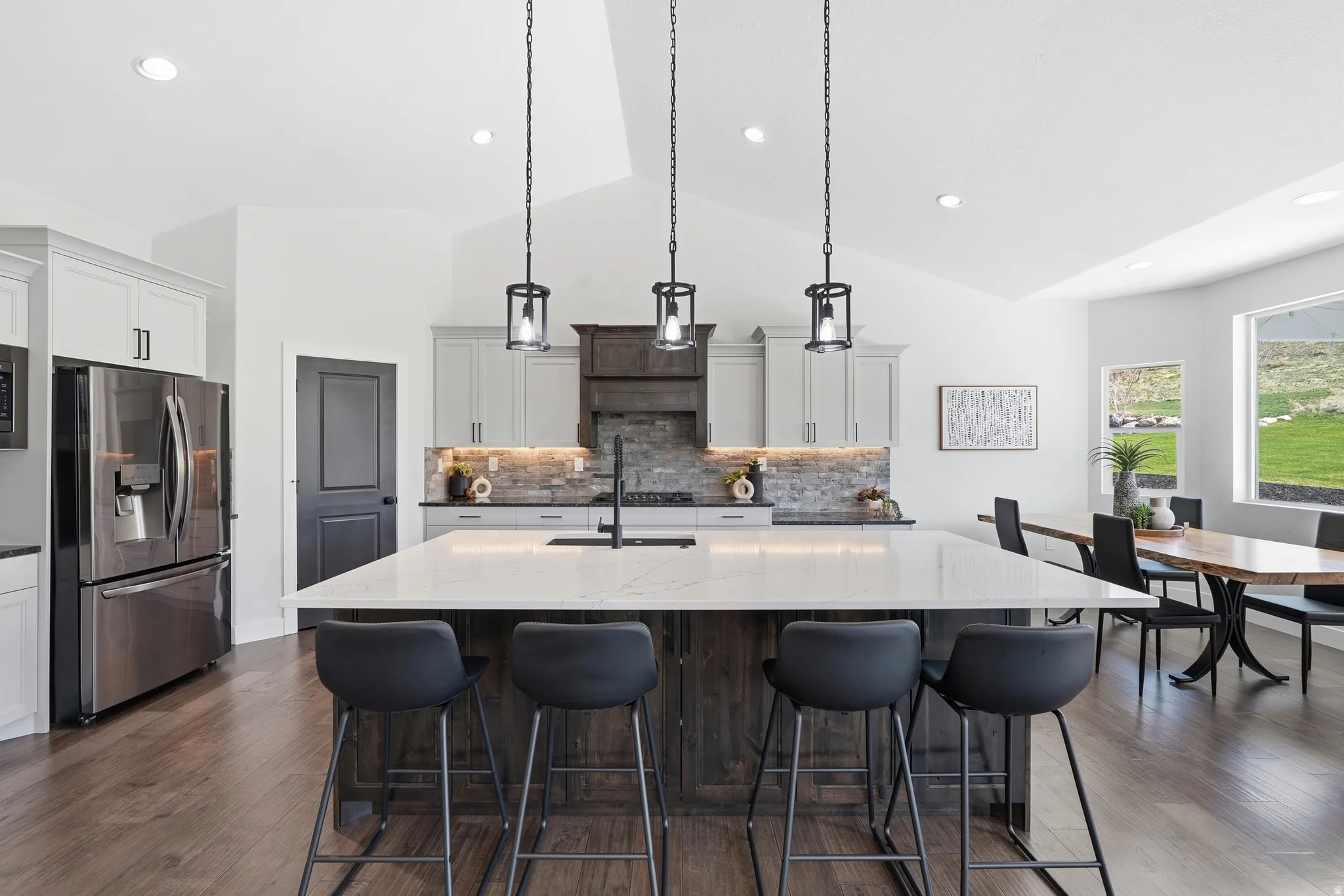 Kitchen with light granite counters, dual tone cabinetry, stainless steel appliances, hanging light fixtures, and hardwood flooring