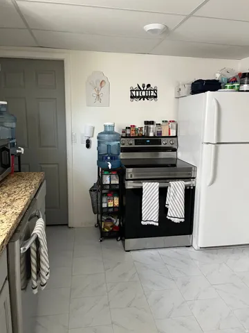 Kitchen featuring stainless steel appliances, a drop ceiling, light marble finish flooring, and light stone countertops