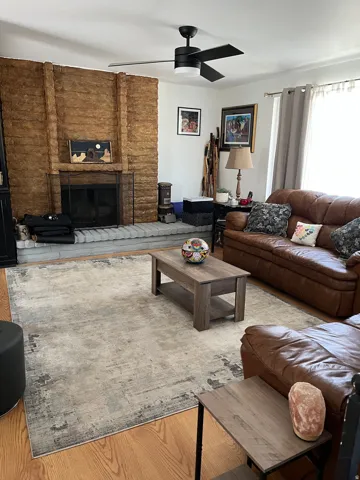 Living area with a ceiling fan, wood finished floors, and a fireplace