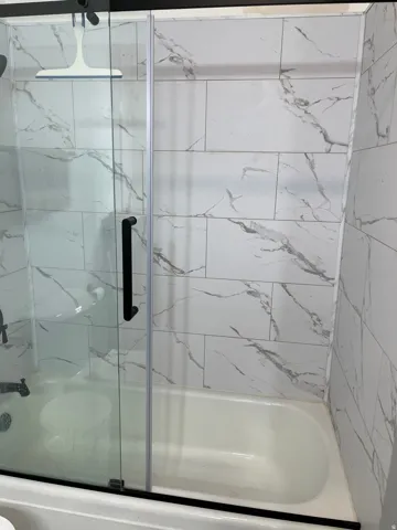 Full bath with a marble finish shower / bath combo